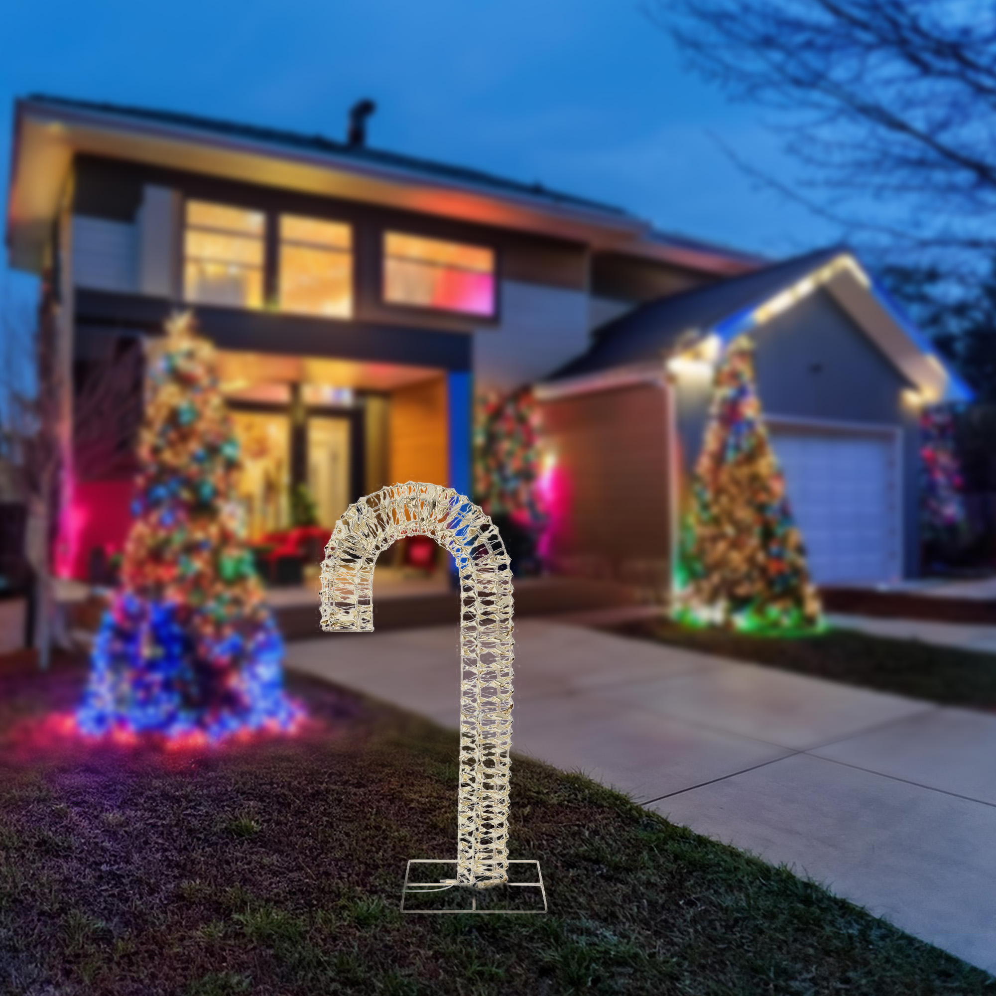 Una decoración de bastón de caramelo iluminado se encuentra frente a una casa decorada para Navidad, con luces de colores.