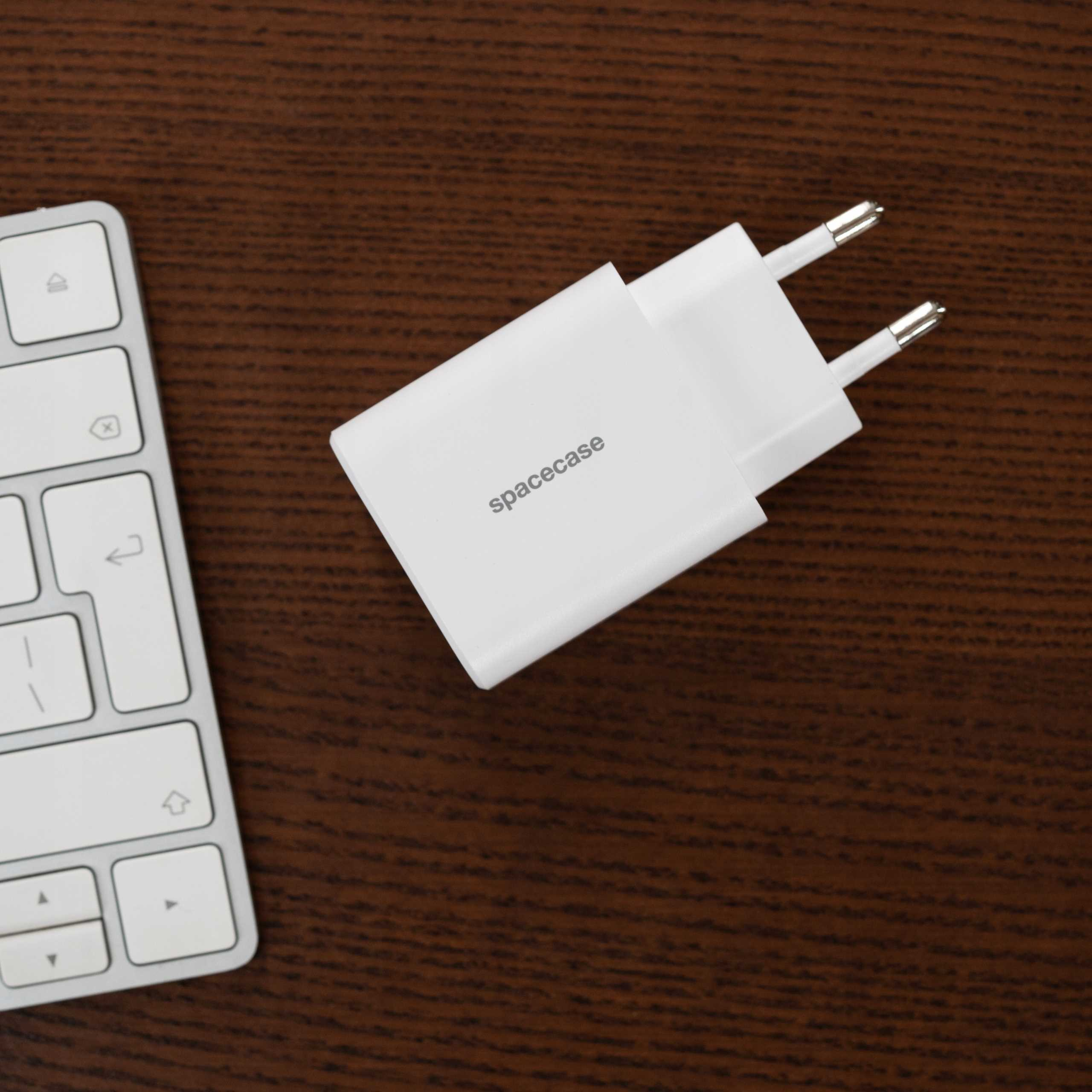 Biała ładowarka, marki 'spacecase', i klawiatura na drewnianej powierzchni.