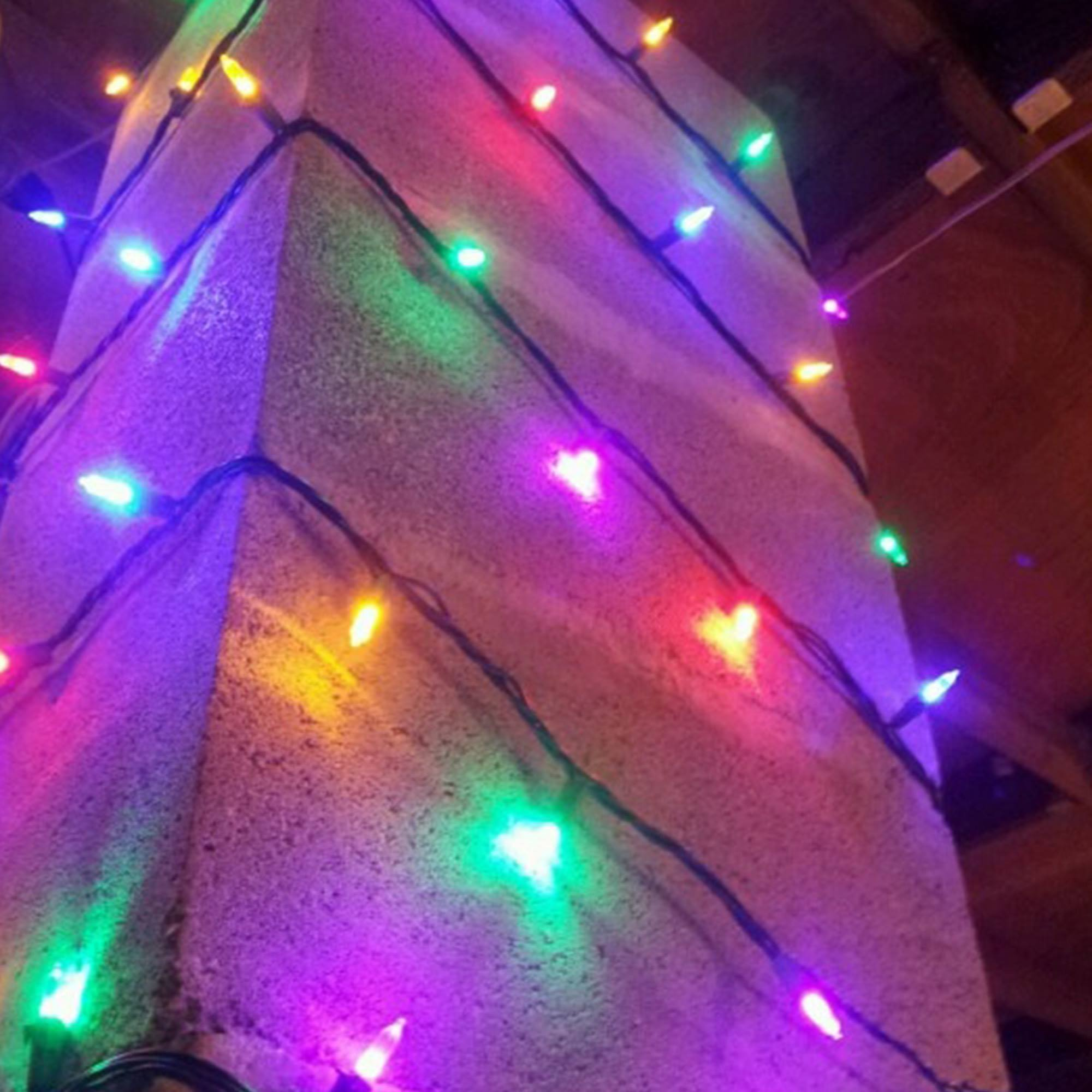 Un pilar de piedra decorado con luces de colores como verde, rosa, amarillo y azul. Fondo oscuro.