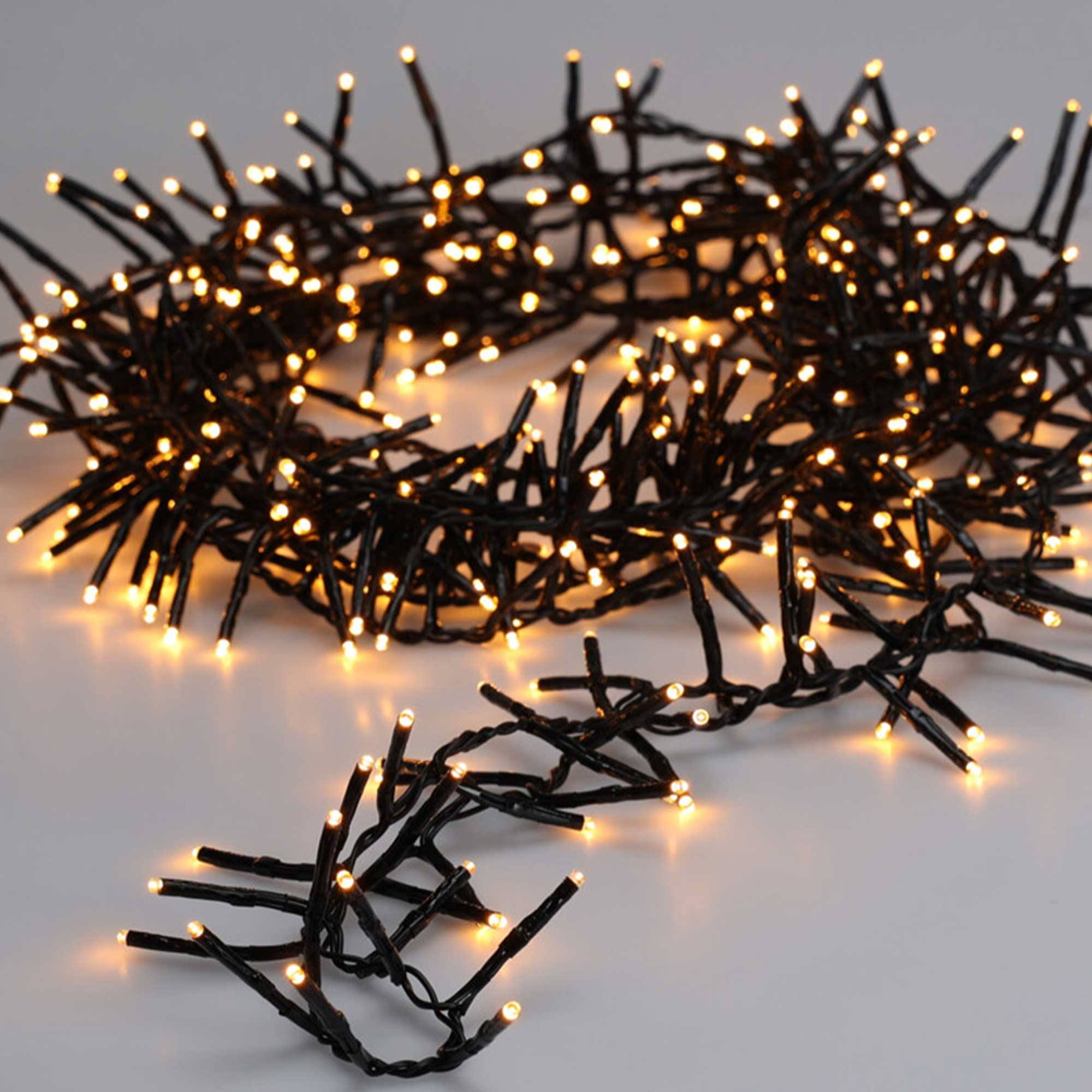 Primer plano de una cadena de luces navideñas blanco cálido sobre una superficie blanca. Las luces están agrupadas.
