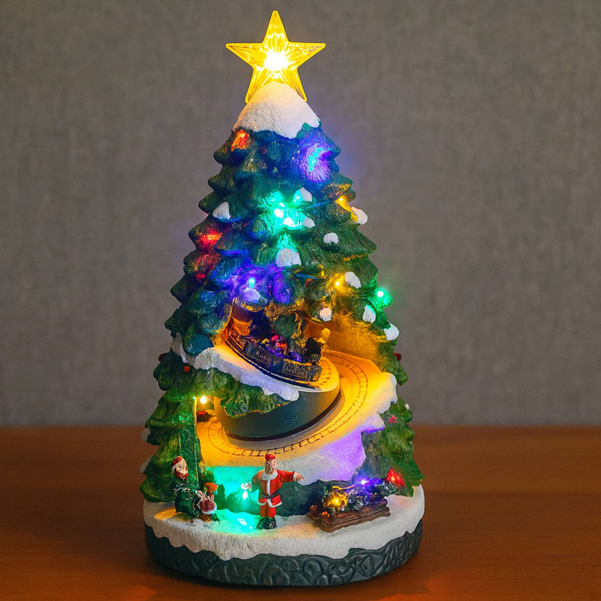 Un adorno de árbol de Navidad con luces, un tren en círculo y Santa. Tiene una estrella encima y nieve.