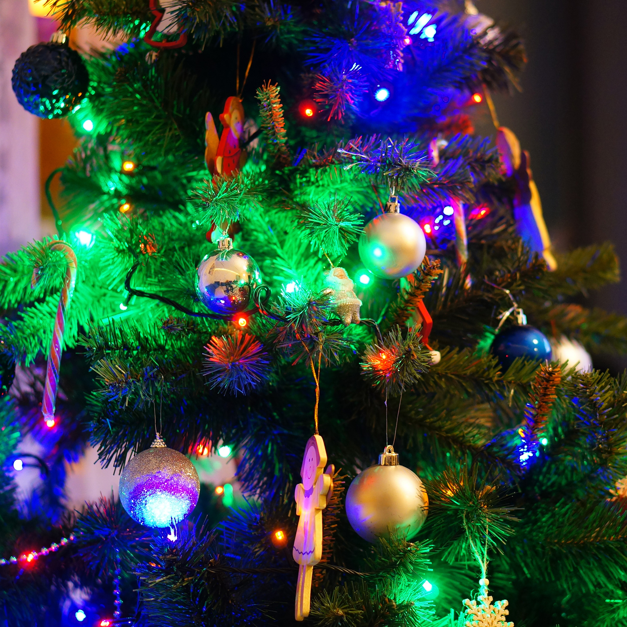 Un árbol de Navidad decorado con adornos, luces y un bastón de caramelo. El fondo es oscuro y borroso.