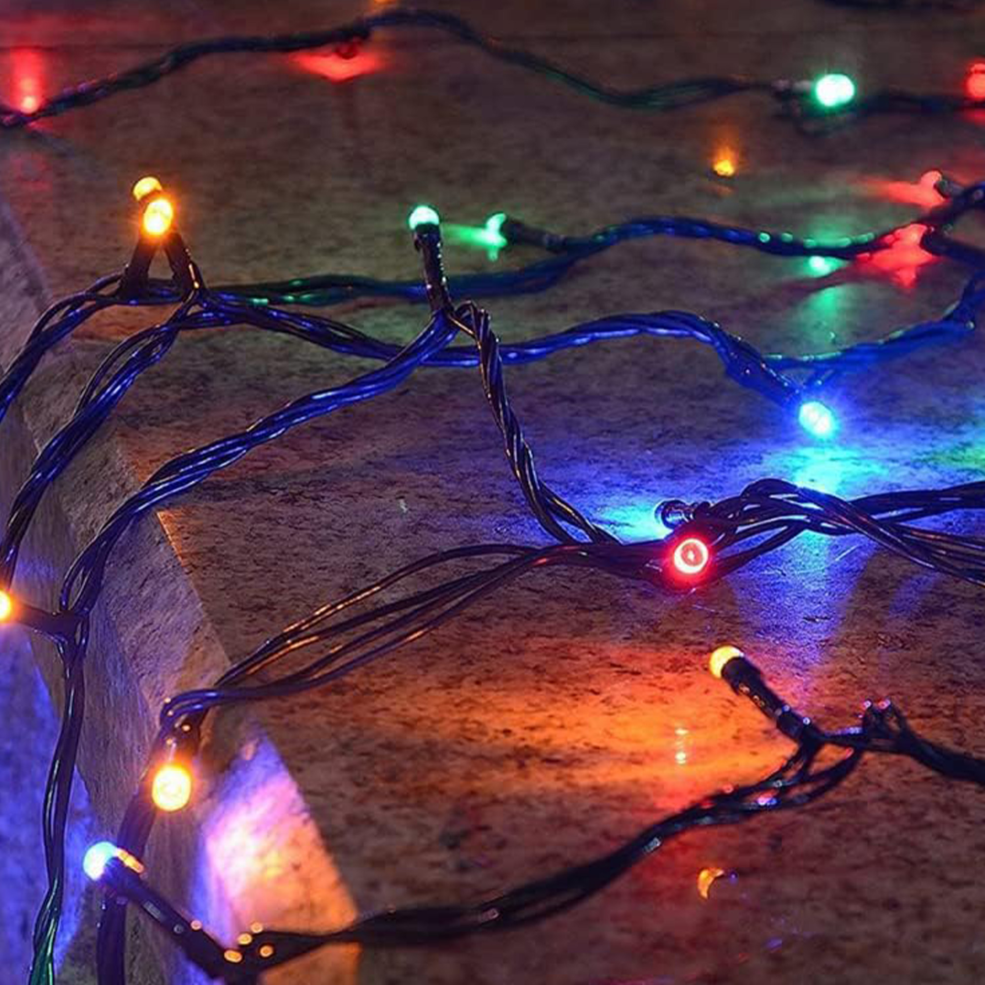 Primer plano de luces de cadena coloridas con luces rojas, verdes, azules y amarillas sobre una superficie oscura.