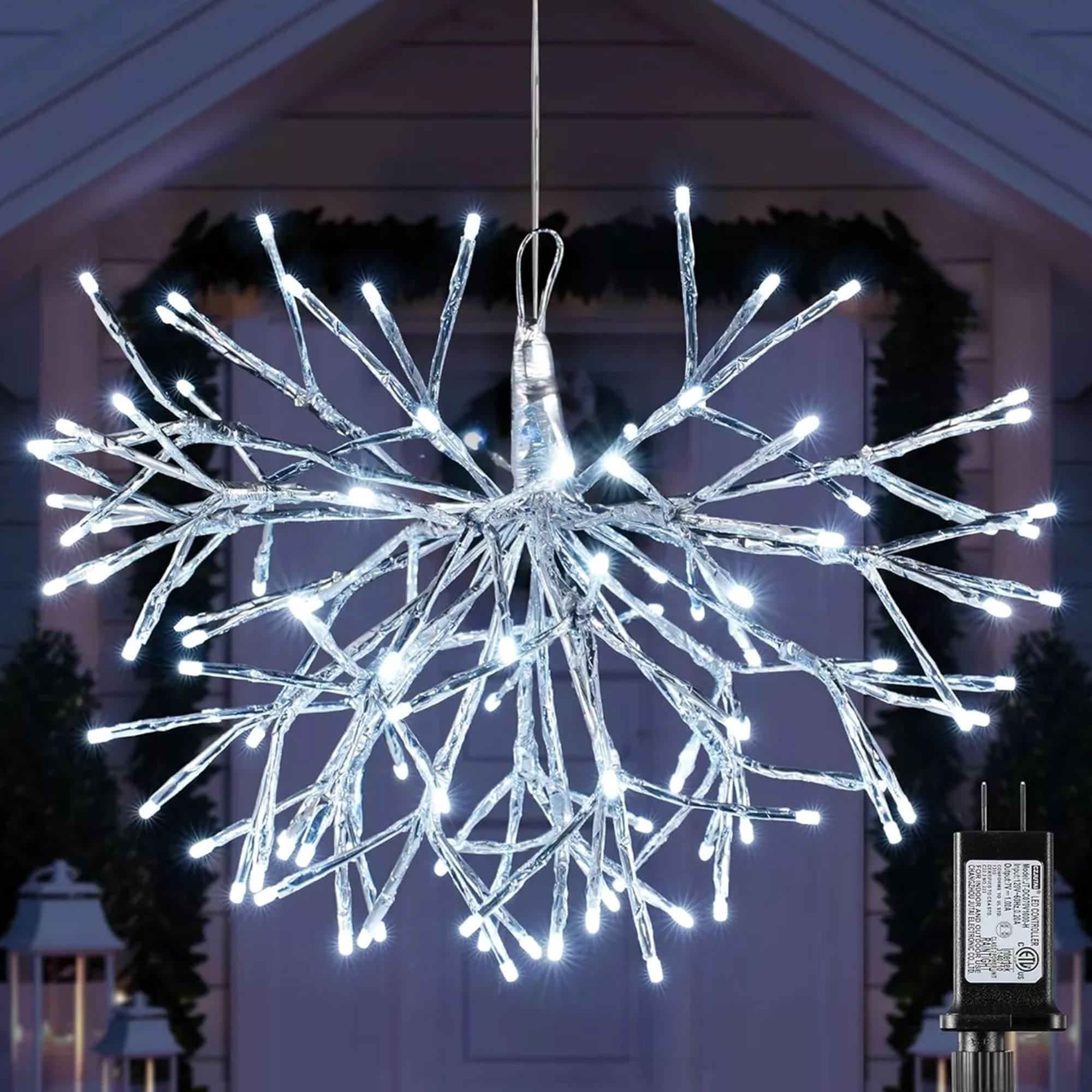 Una lámpara de luces en forma de estrella con muchas luces blancas, colgando frente a una casa. Un adaptador de corriente es visible a la derecha.