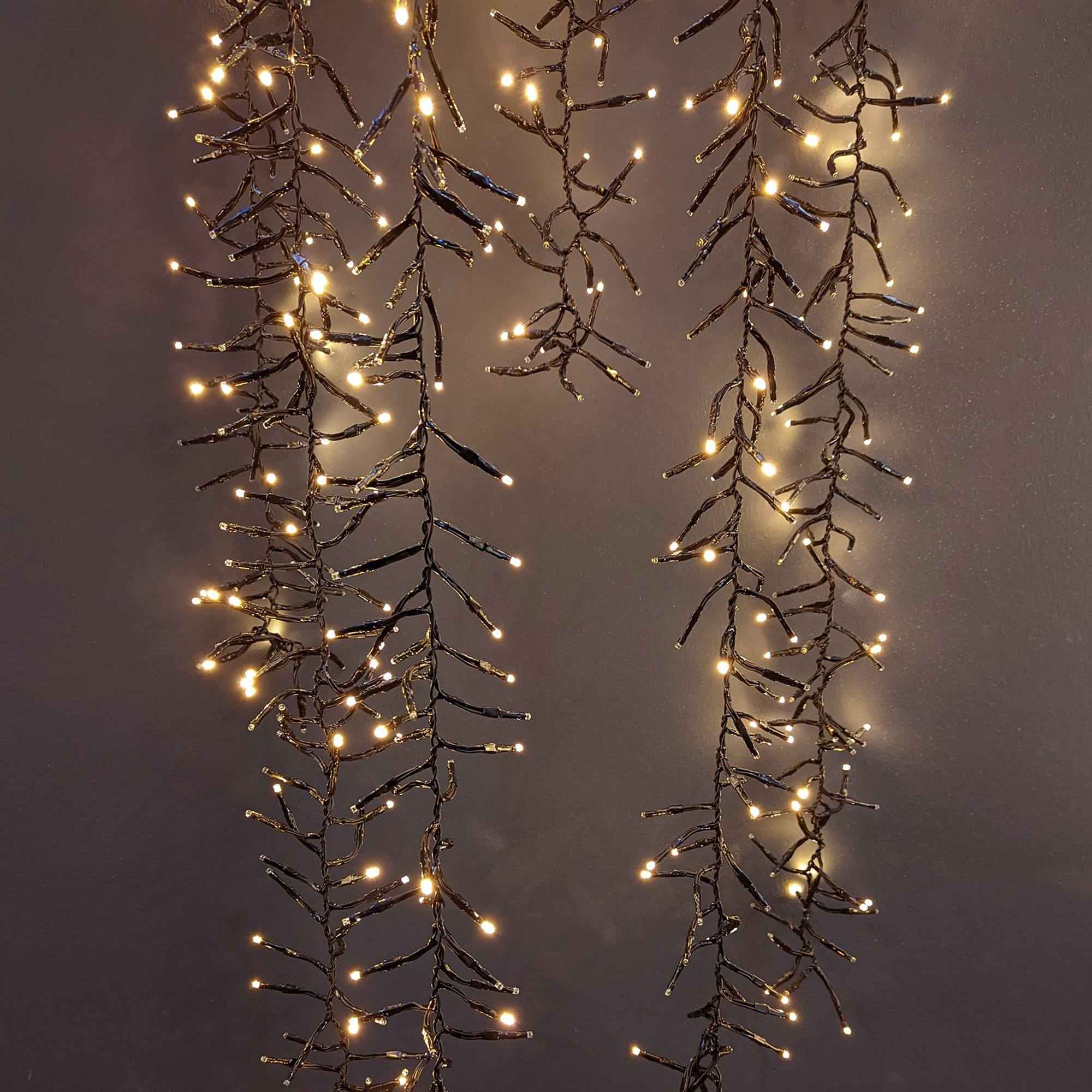 Luces de cadena con pequeñas bombillas blanco cálido cuelgan sobre un fondo gris oscuro, creando un ambiente festivo y acogedor.
