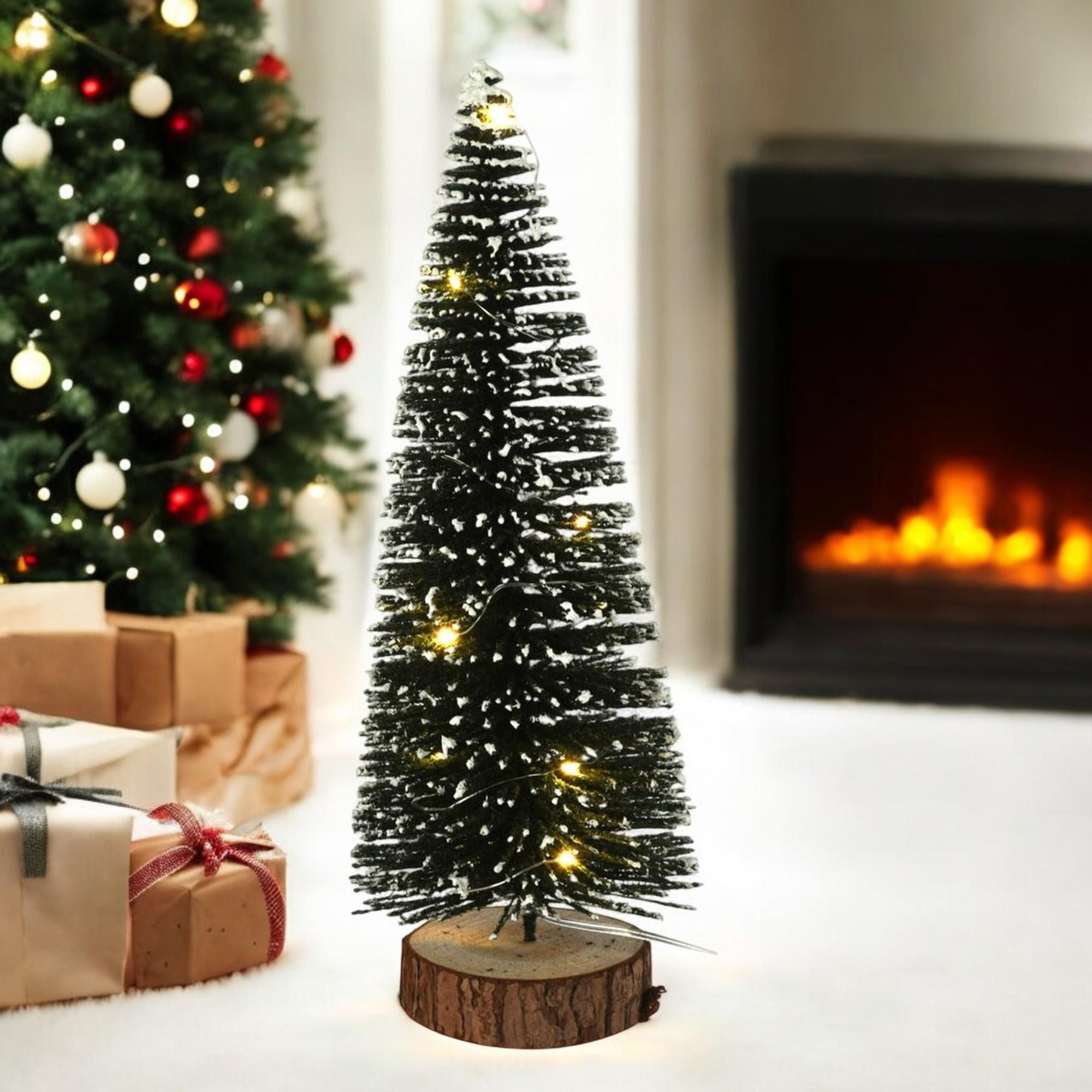 Un pequeño árbol de Navidad con luces está frente a una chimenea. Hay regalos a la izquierda.