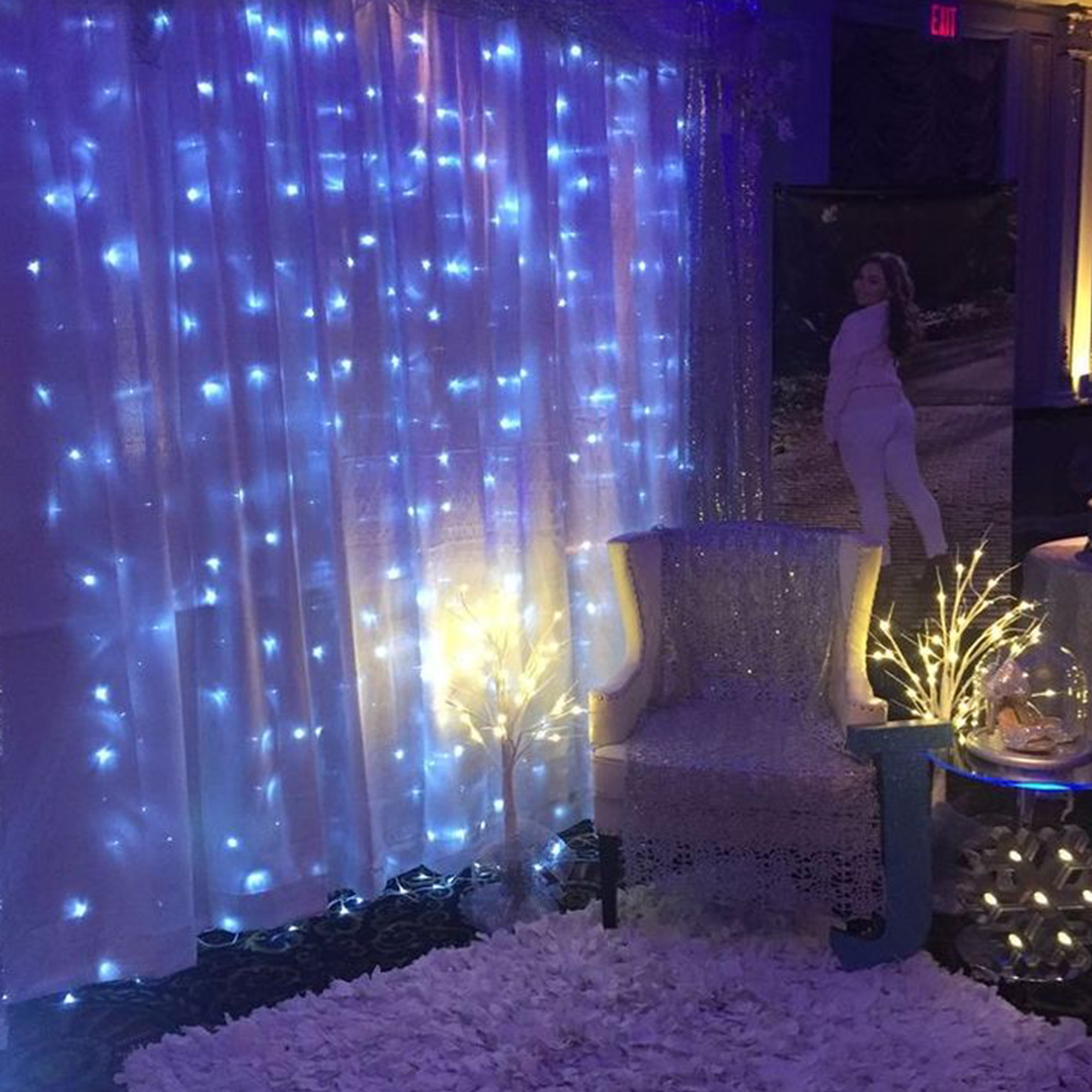 Una habitación con luces de hadas azules, una silla, una persona y una alfombra mullida. Un árbol con luces en el centro.