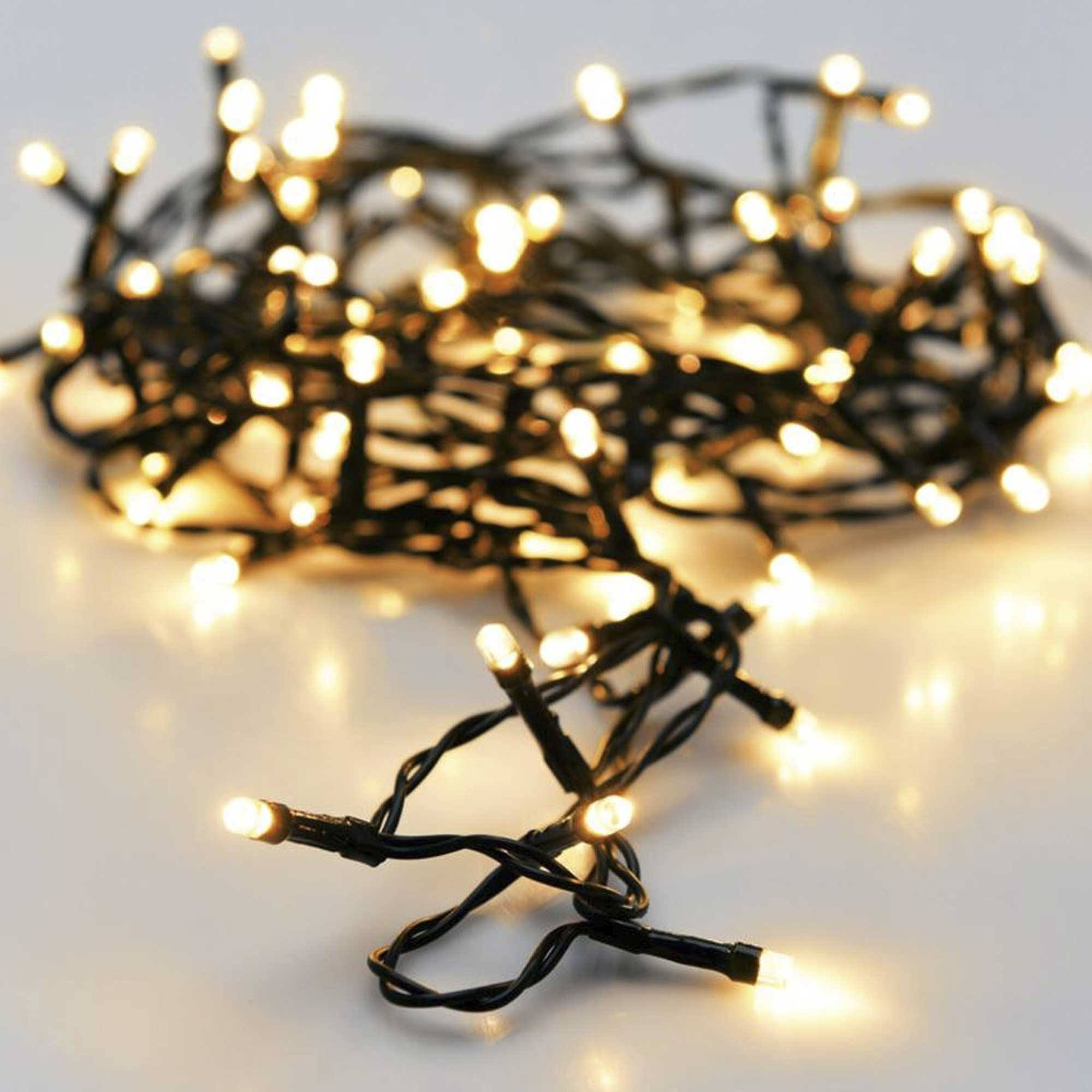 Primer plano de luces navideñas. Luces blancas cálidas sobre alambre negro, dispersas sobre una superficie blanca. Algunas luces enfocadas.