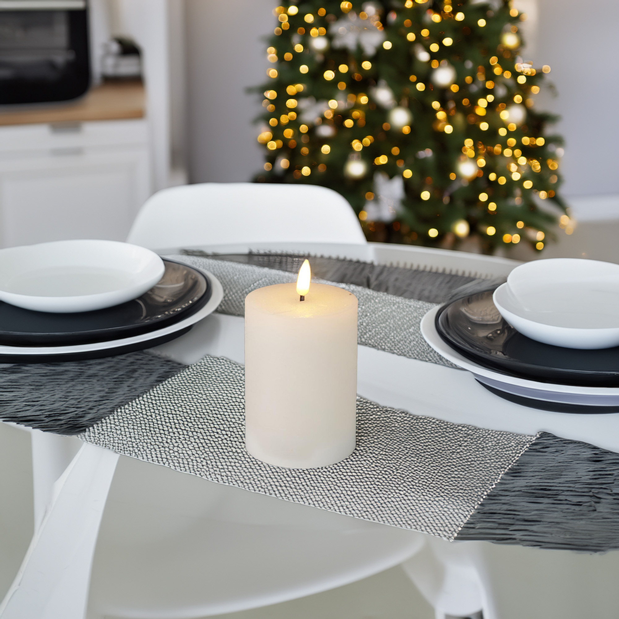 Una vela encendida sobre una mesa para una comida. Un árbol de Navidad con luces está en el fondo.