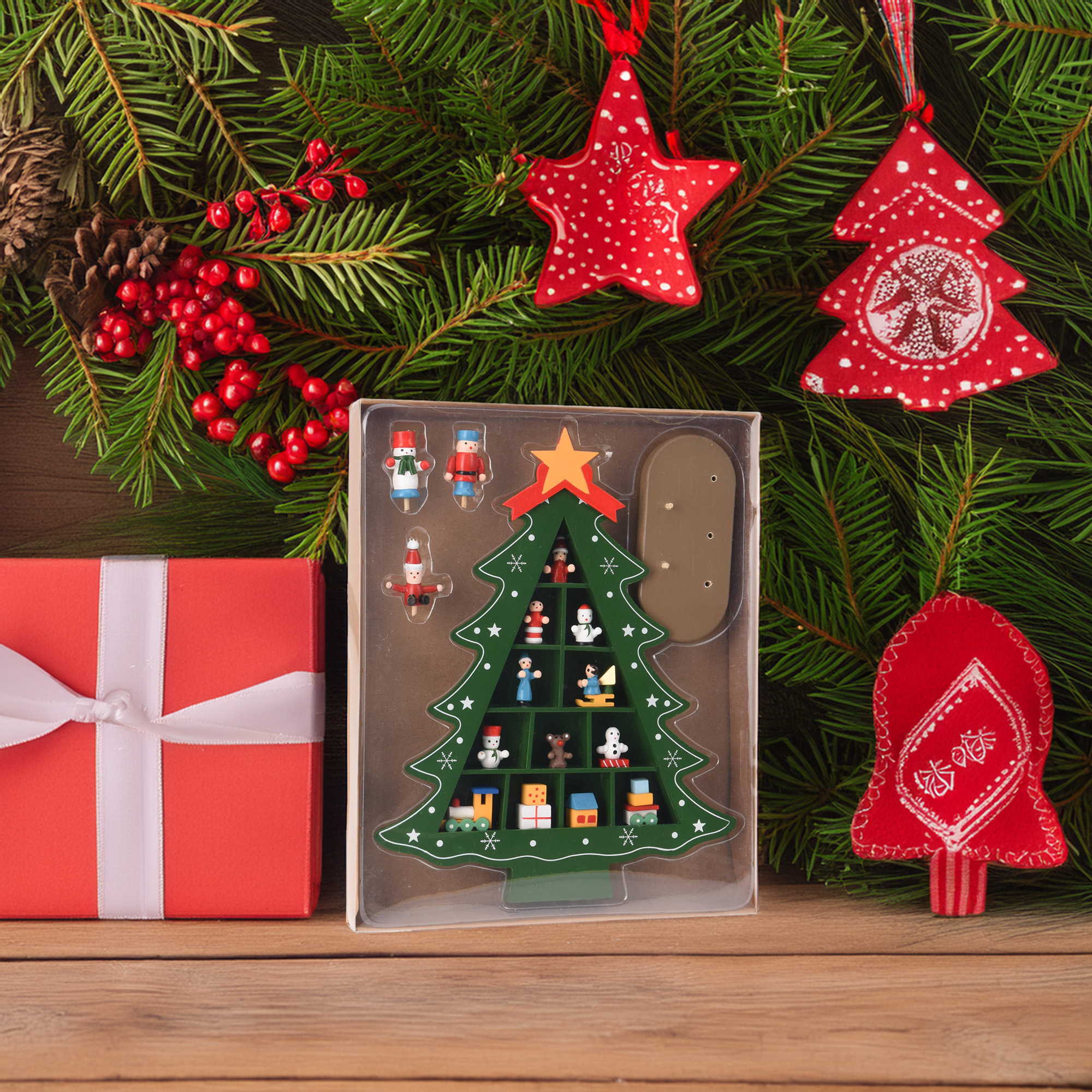 Escena festiva con caja de regalo roja, adornos y decoración de árbol de Navidad sobre fondo de ramas de abeto.