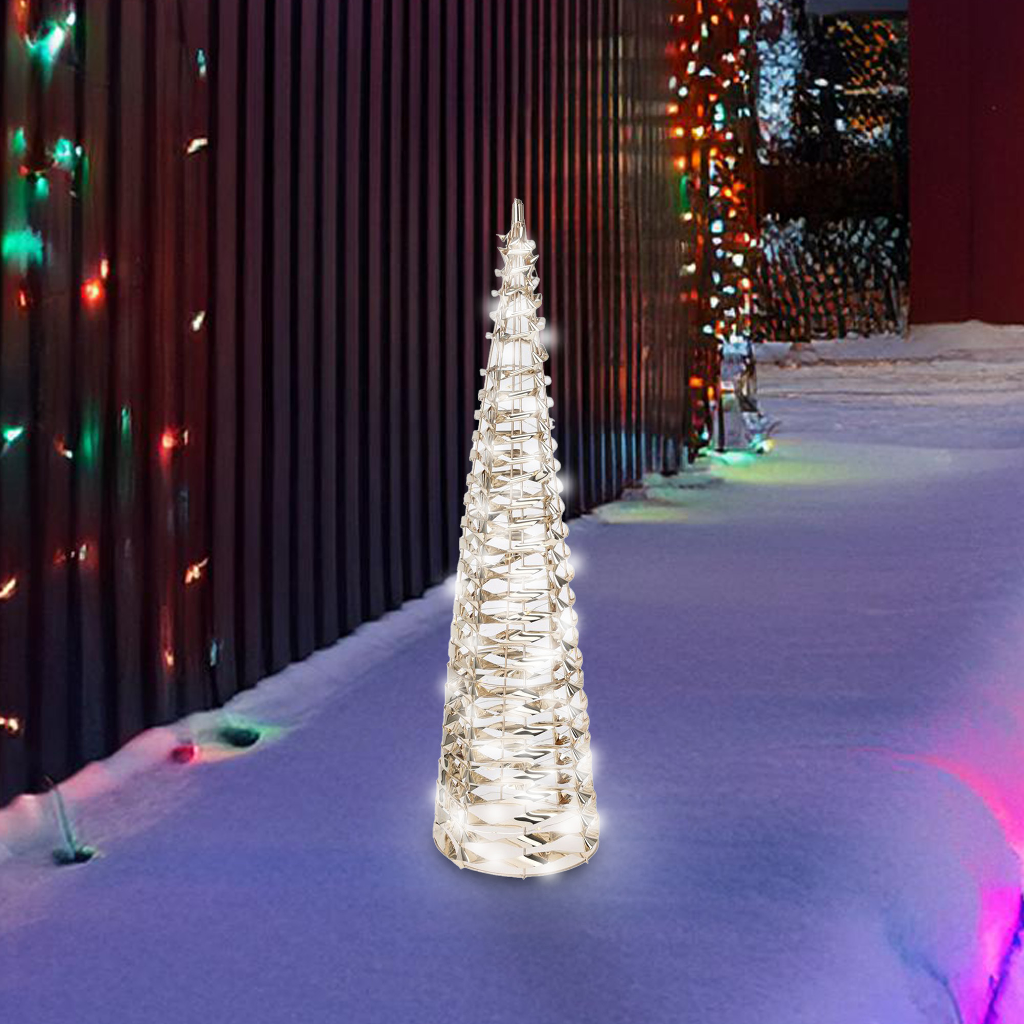 Una decoración de árbol de Navidad iluminada está en la nieve. Una valla oscura y luces de cadena están en el fondo.