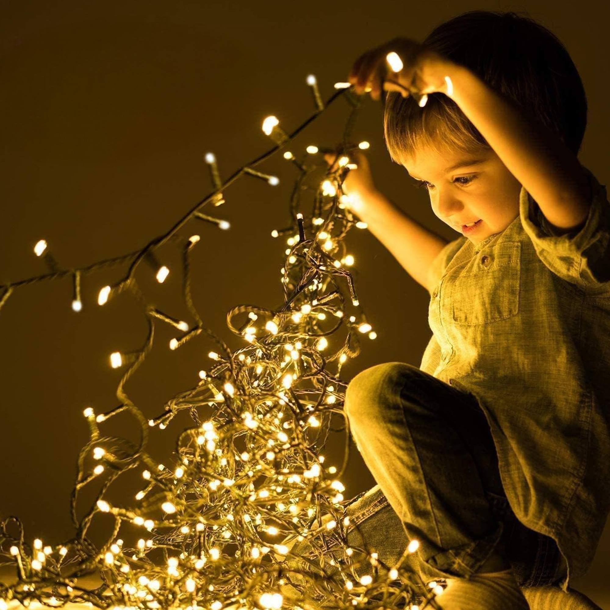 Un niño sostiene luces de cadena, iluminadas contra un fondo cálido. La cara del niño muestra alegría. Las luces son brillantes.
