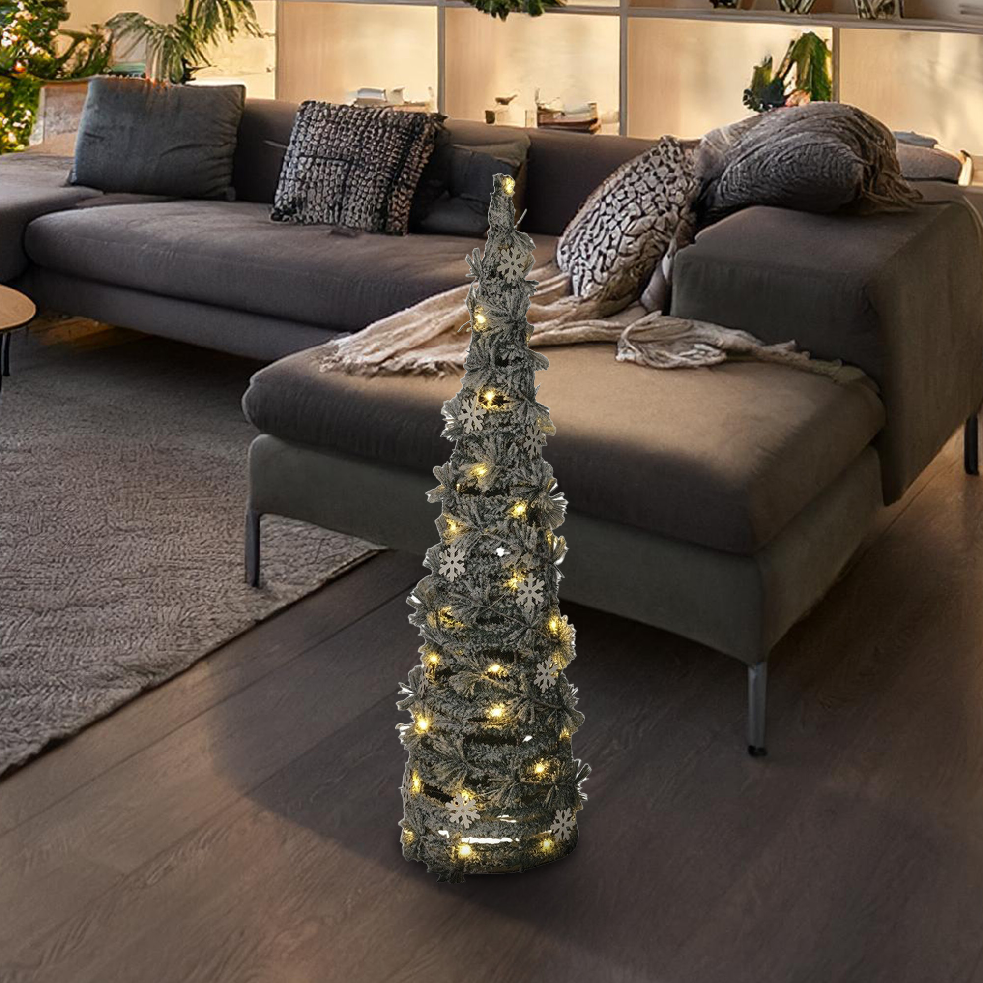 Un árbol de Navidad iluminado con copos de nieve en una sala de estar. Un sofá gris en el fondo.