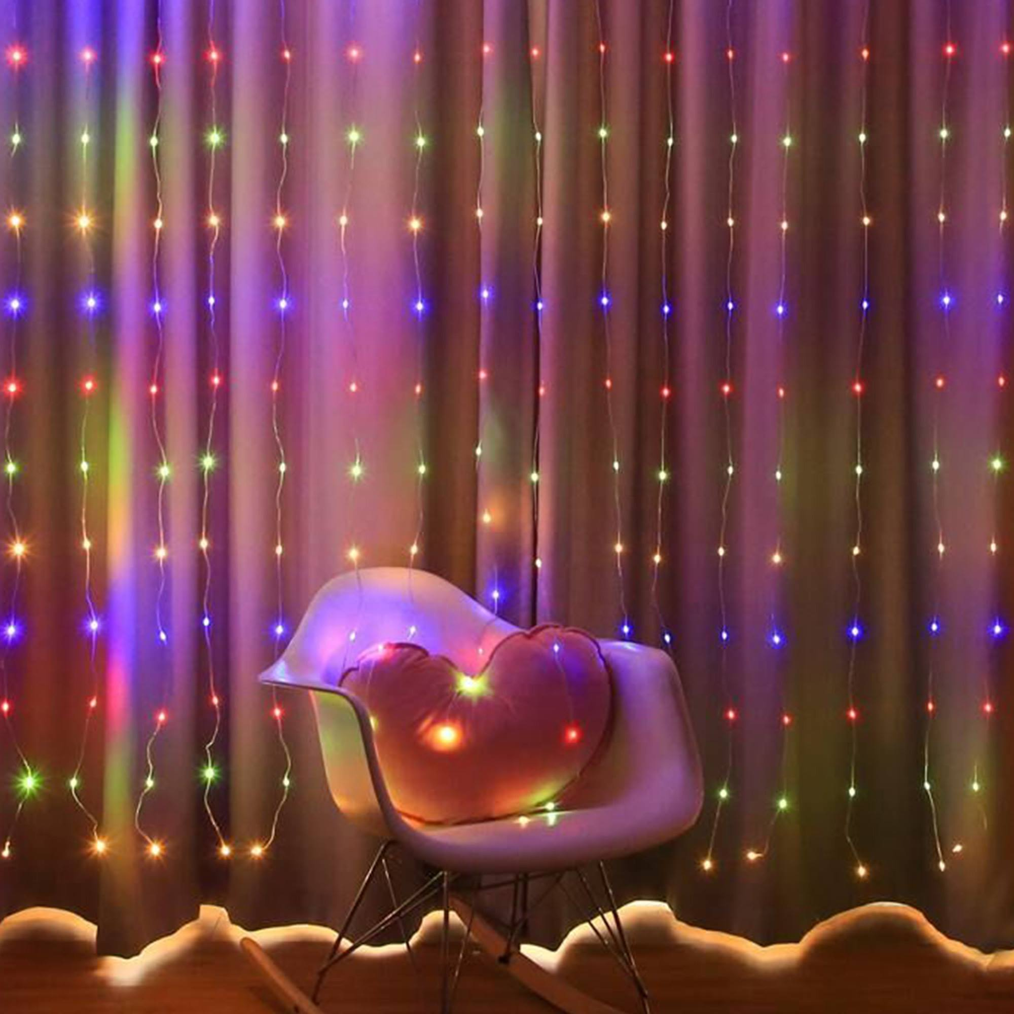 Cortina de luces de colores detrás de una silla blanca con una almohada en forma de corazón. El fondo es una cortina morada.