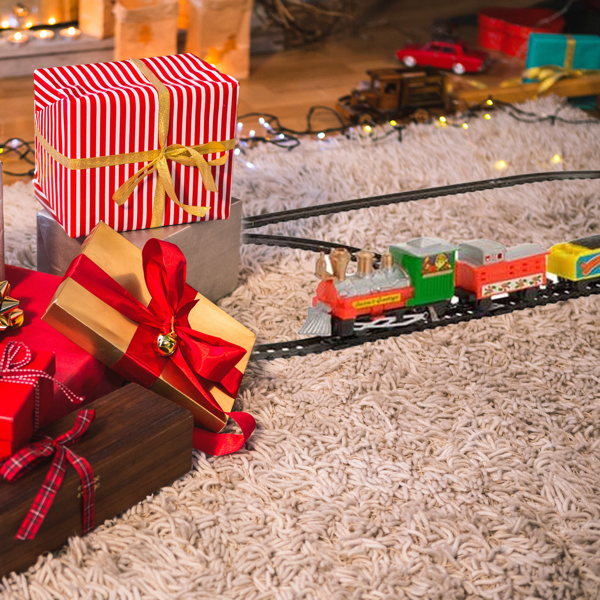 Escena navideña con regalos envueltos y un tren de juguete sobre una alfombra esponjosa. Regalos en rojo y dorado. El tren es colorido.