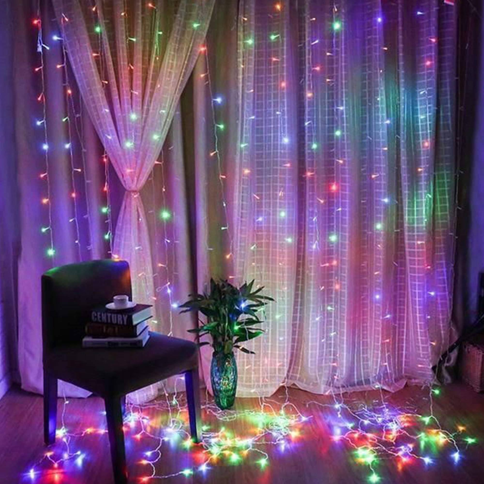 Una habitación con luces de hadas de colores colgando del techo. Una silla con libros y una planta en primer plano.