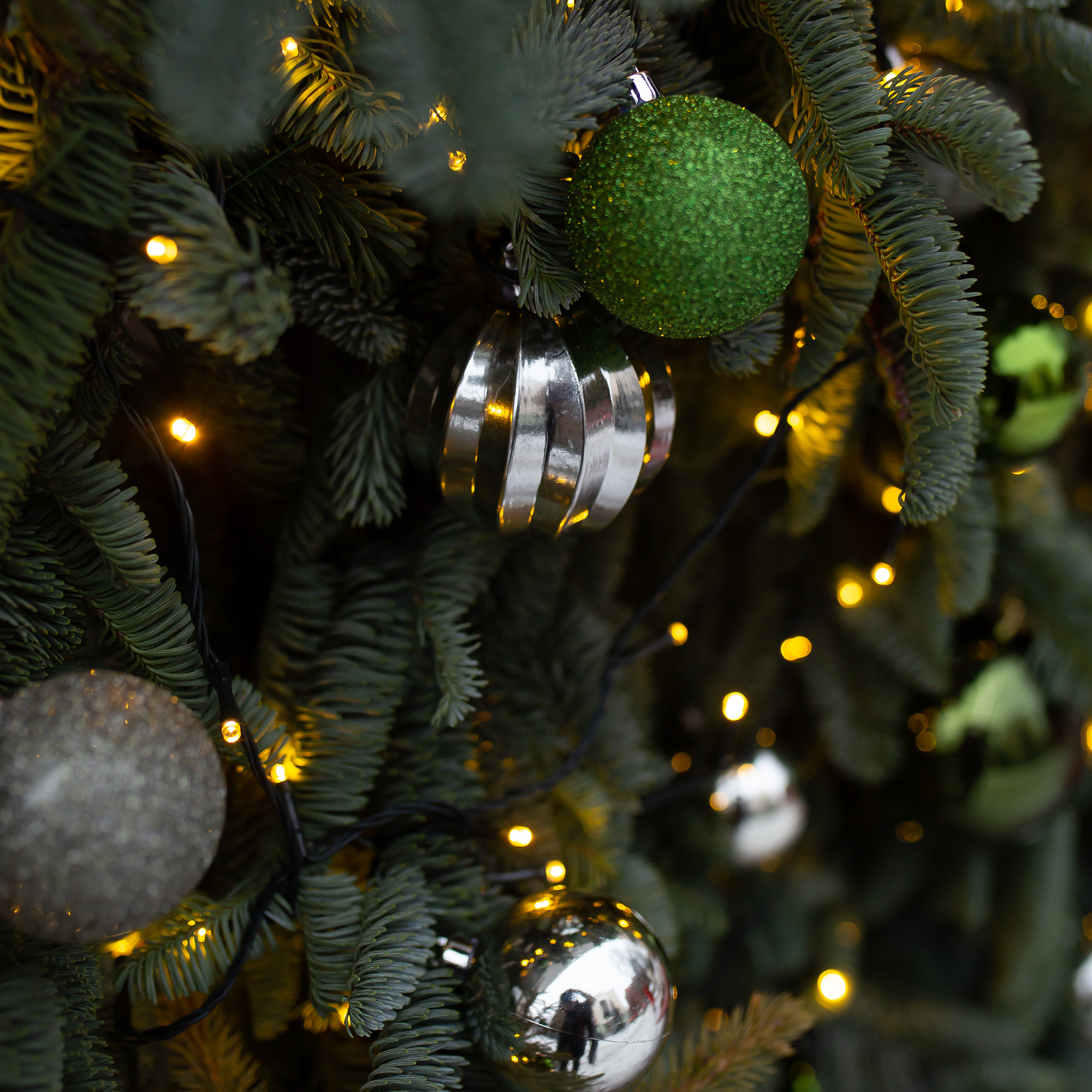 Primer plano de un árbol de Navidad con adornos, incluyendo bolas verdes, plateadas y luces.