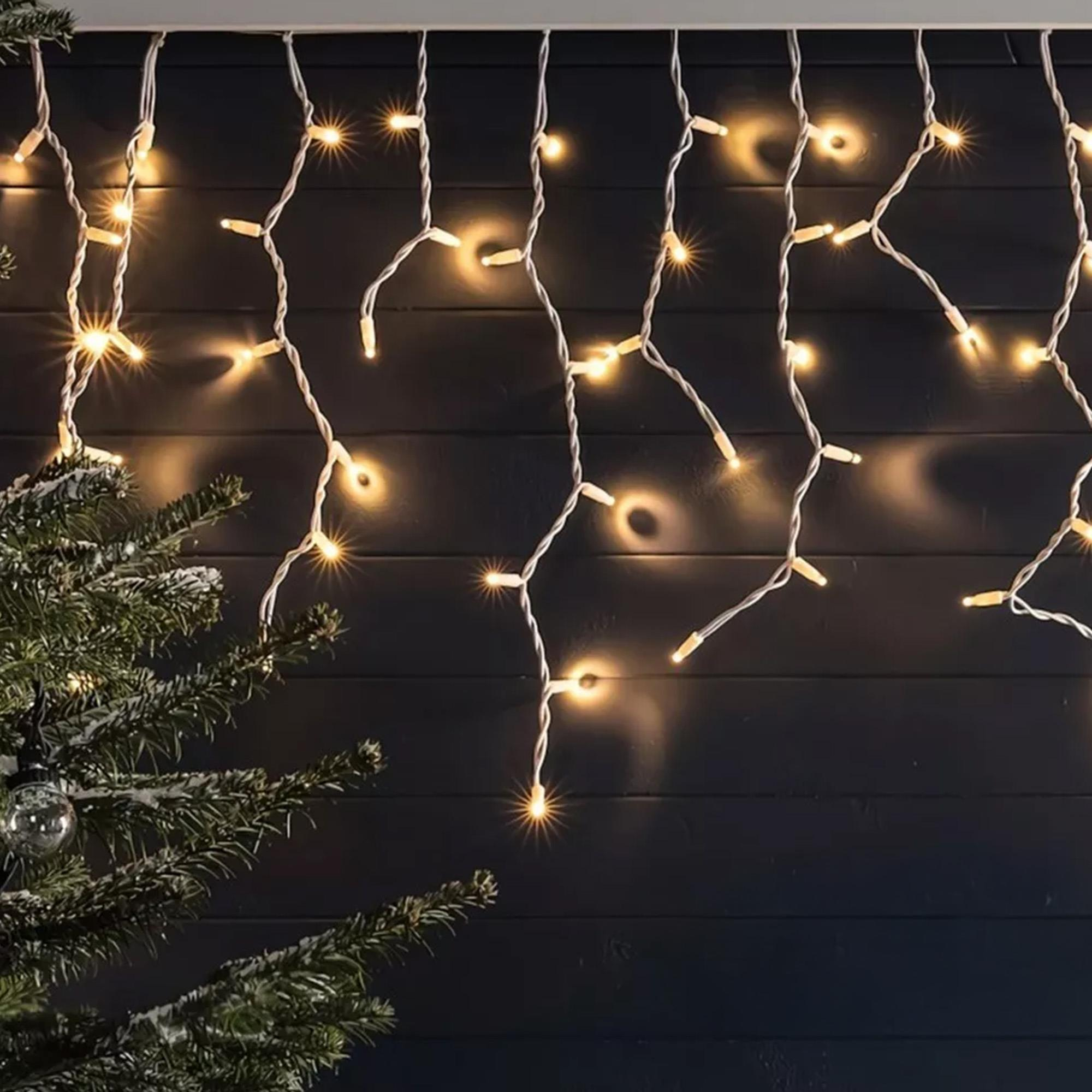 Luces de cadena cuelgan con una rama de árbol de Navidad a la izquierda. Fondo de pared negra. Luces amarillas cálidas.
