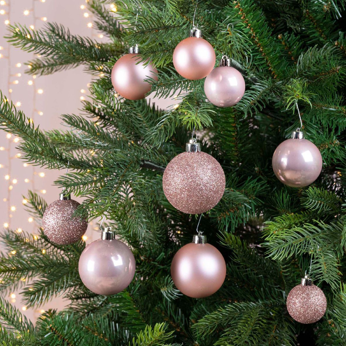 Un árbol de Navidad adornado con varios adornos de oro rosa. Algunos son brillantes, otros lisos, colgando sobre un fondo suave y borroso.