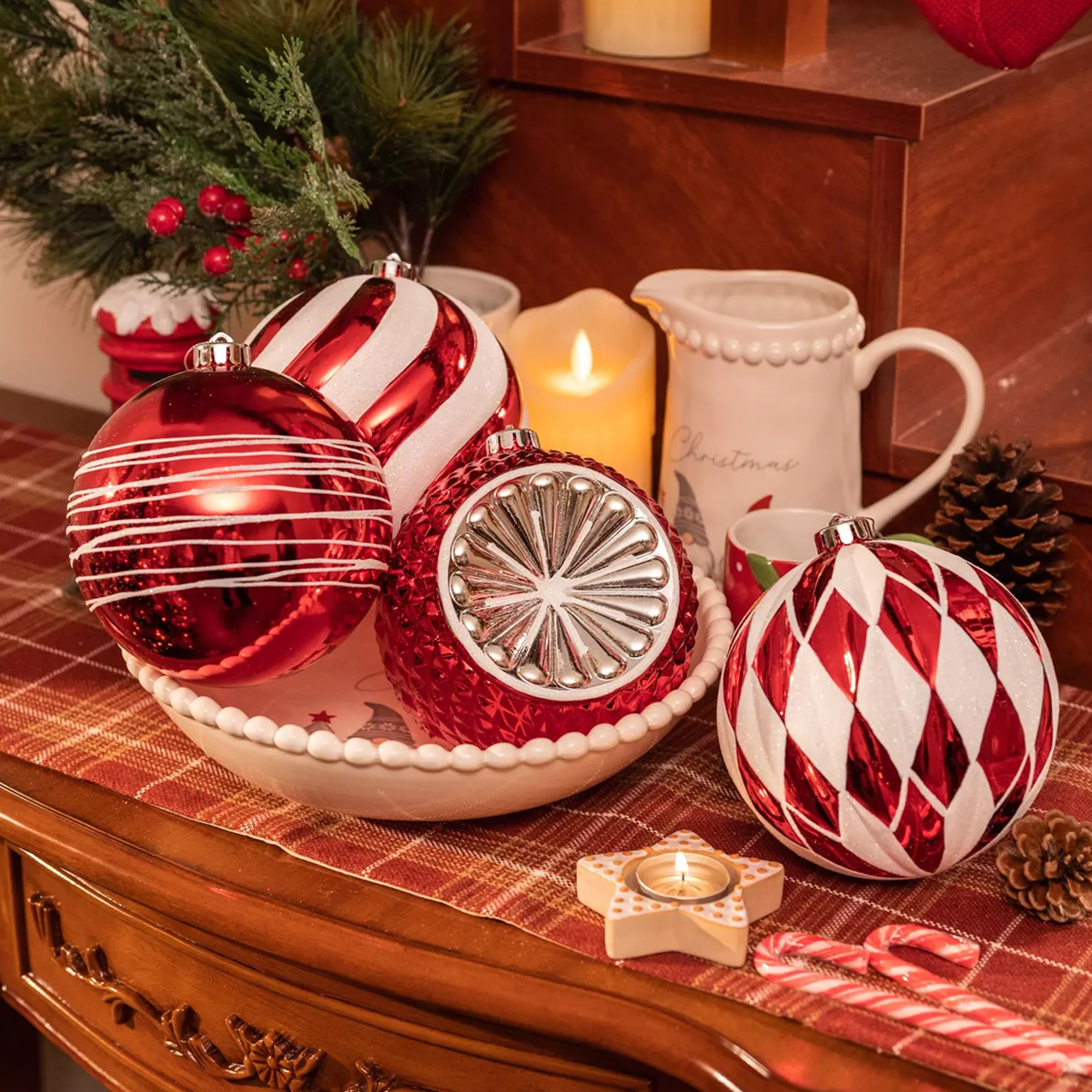 Decoraciones navideñas: adornos rojos y blancos, velas, pino, bastones de caramelo y un portavelas de estrella sobre una mesa de madera.