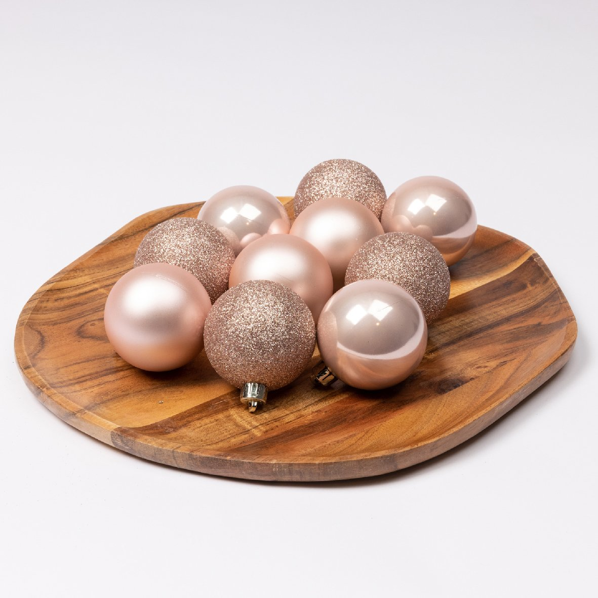 Nueve adornos navideños rosas, algunos brillantes, sobre una bandeja de madera contra un fondo blanco.