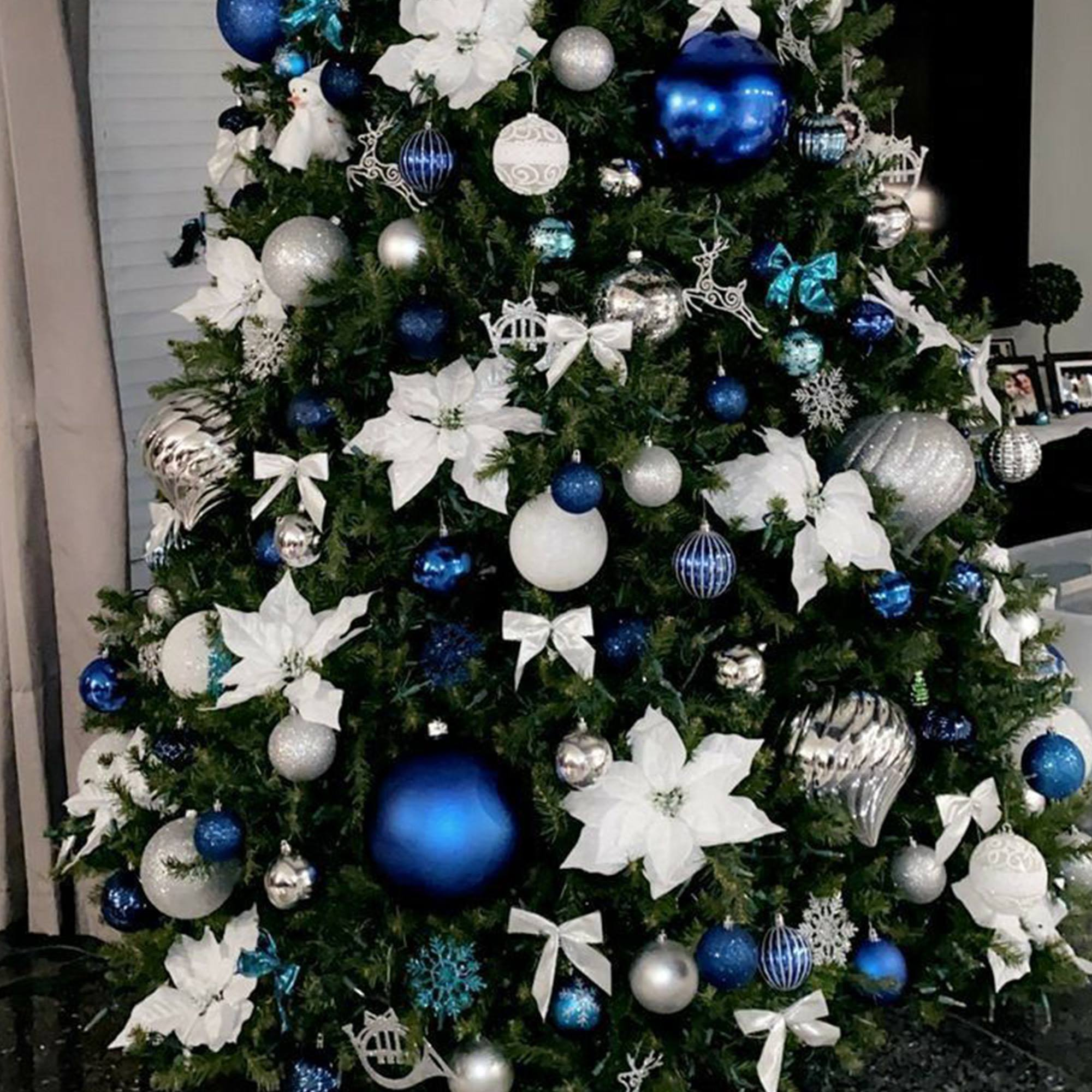 Árbol de Navidad con adornos azules y plateados, flores blancas y lazos. Muñeco de nieve en la cima. Fondo oscuro.