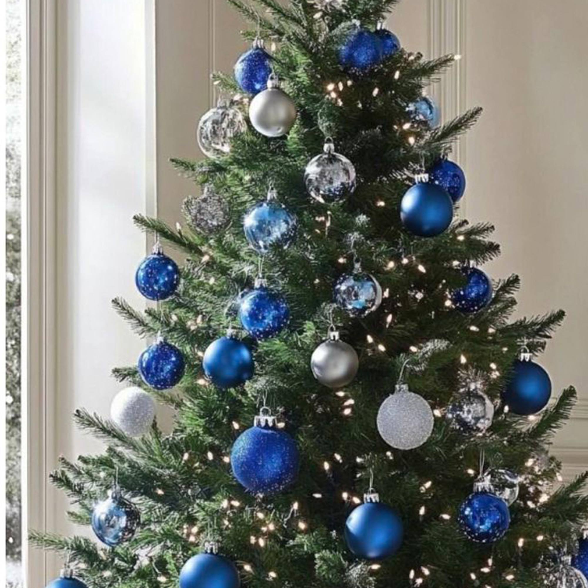 Un árbol de Navidad decorado con adornos azules y plateados, iluminado por luces de hadas. El fondo es una ventana.