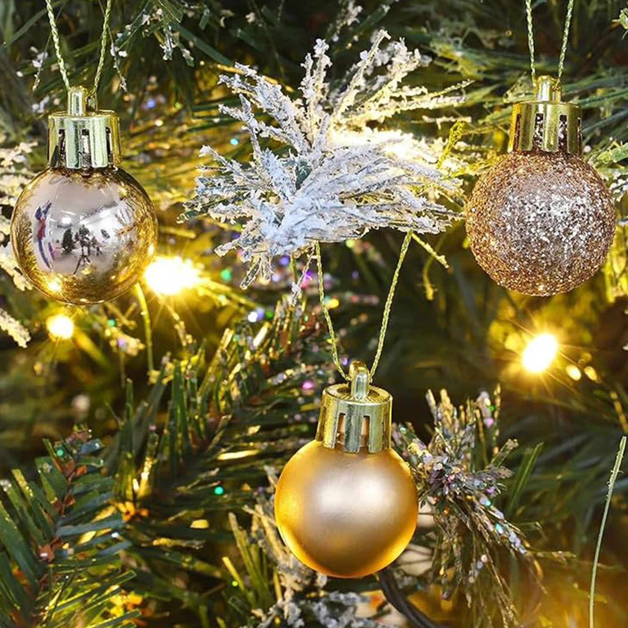 Primer plano de árbol de Navidad con adornos: bolas doradas y una ramita helada.
