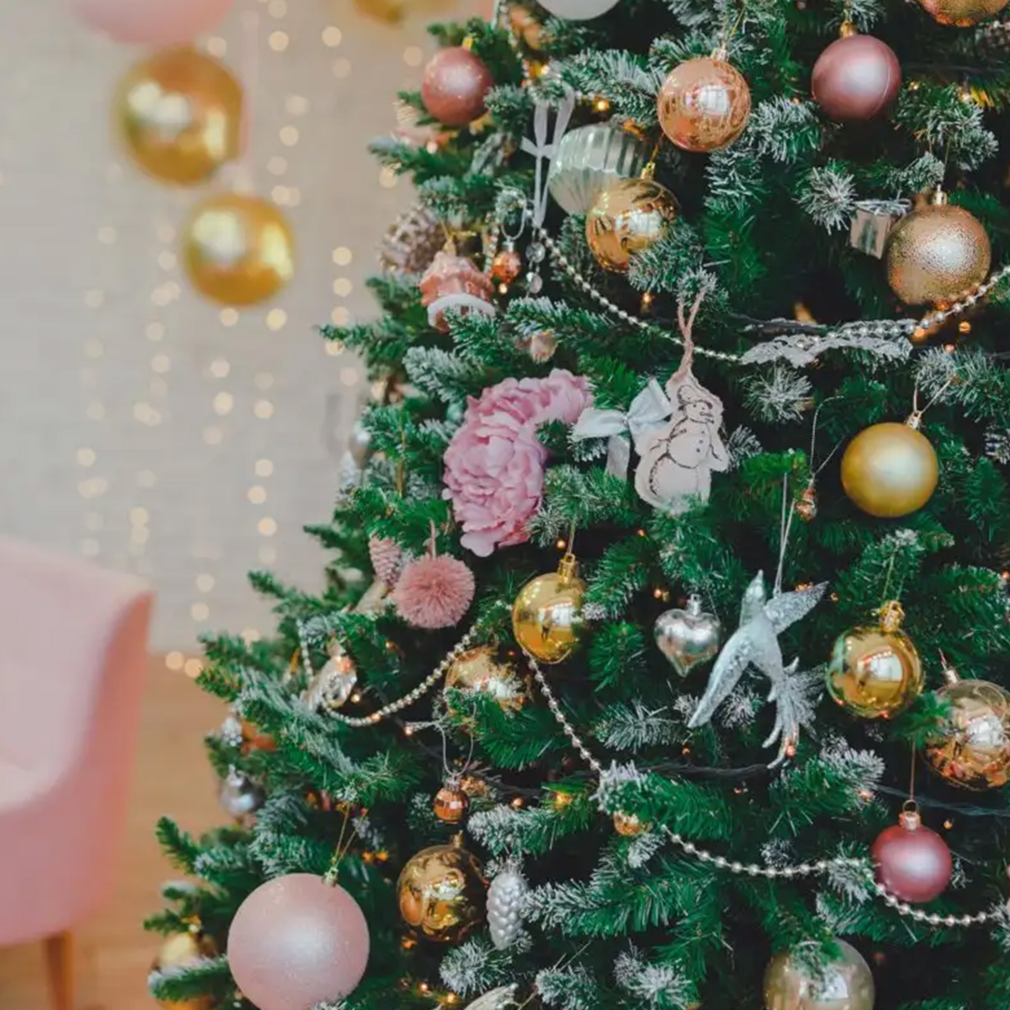 Árbol de Navidad con adornos. Adornos dorados y rosas, decoraciones plateadas, luces de hadas. Una silla rosa al fondo.