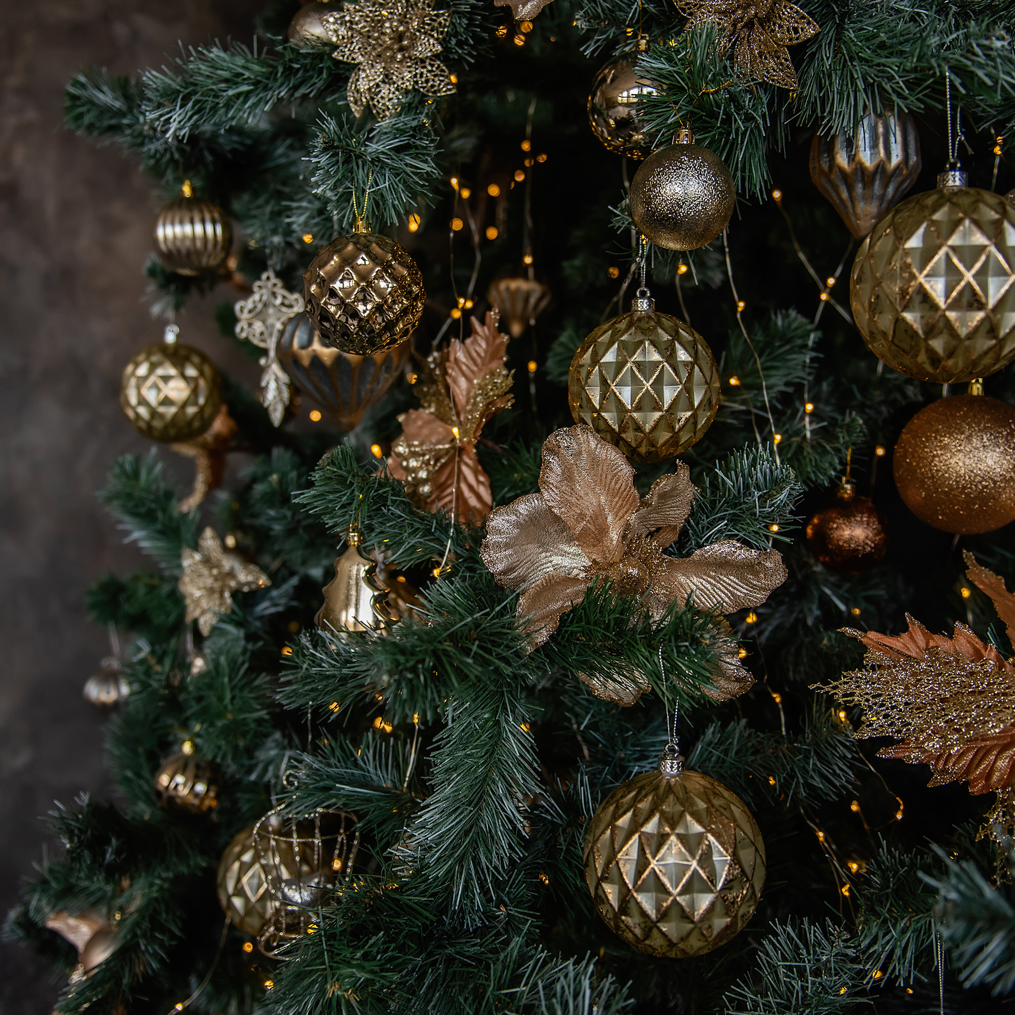 Primer plano de un árbol de Navidad decorado con adornos dorados, luces y un fondo oscuro.