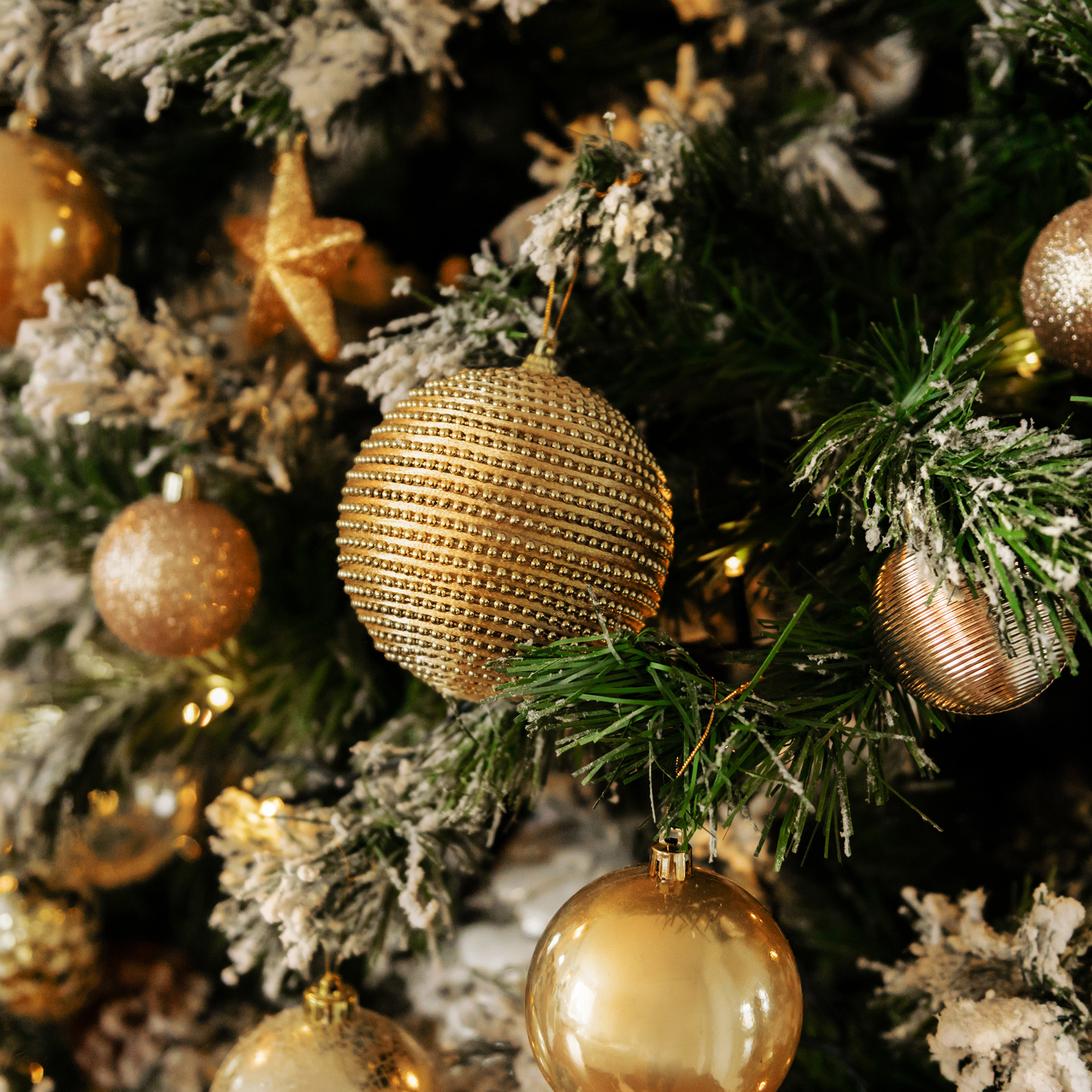 Primer plano de un árbol de Navidad con adornos dorados, incluyendo bolas y una estrella, cubierto de nieve artificial.
