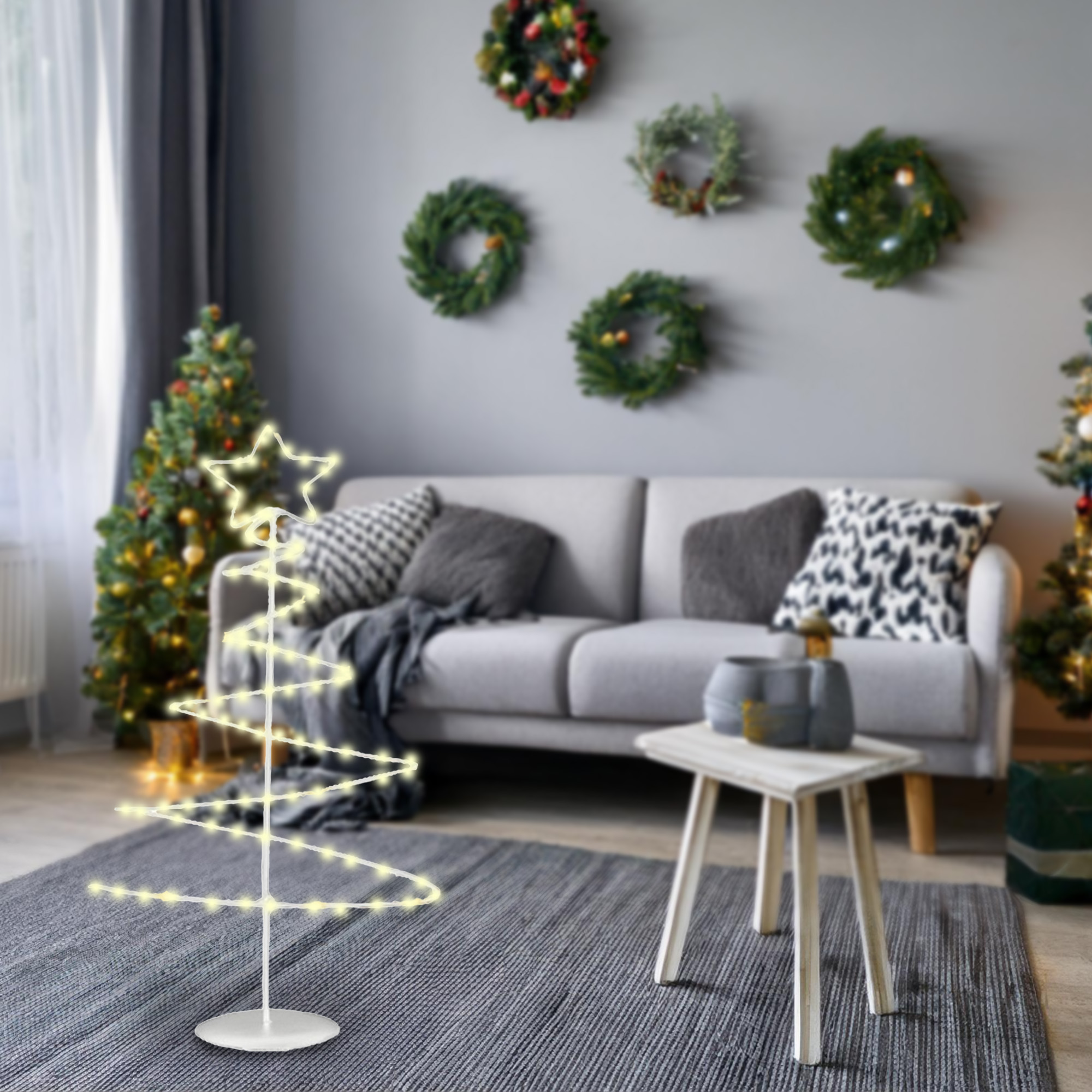 Un salón festivo con un árbol espiral iluminado, árbol de Navidad, coronas, sofá y una mesita.