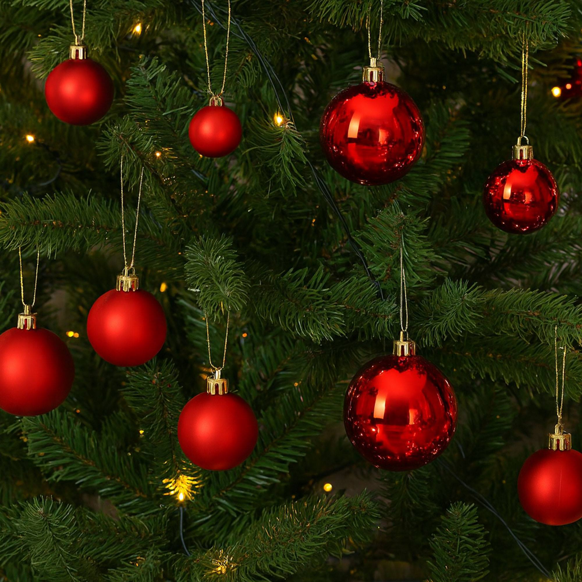 Primer plano de un árbol de Navidad decorado con adornos rojos de varias texturas, colgando de cuerdas doradas en ramas verdes.