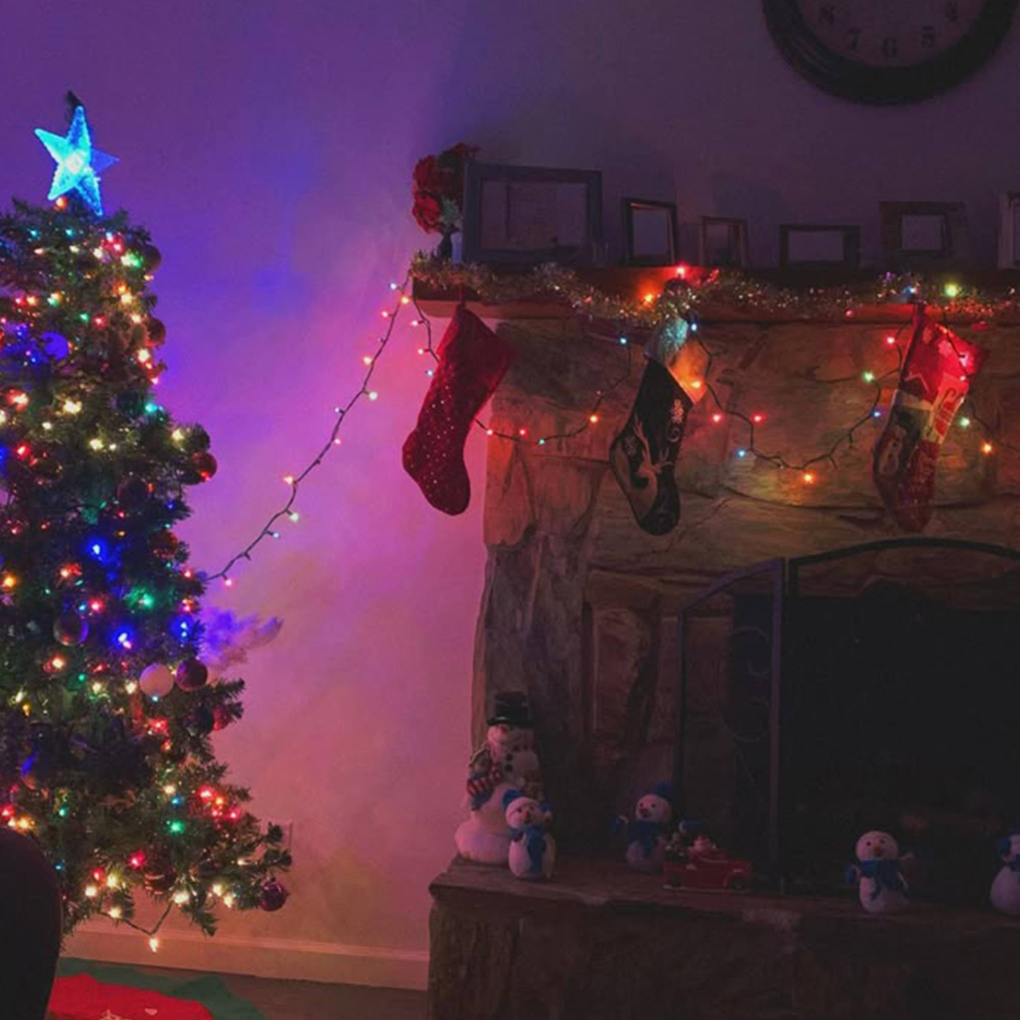 Un árbol de Navidad decorado con una estrella, calcetines en una chimenea y decoraciones de muñecos de nieve. Luces de colores iluminan la escena.