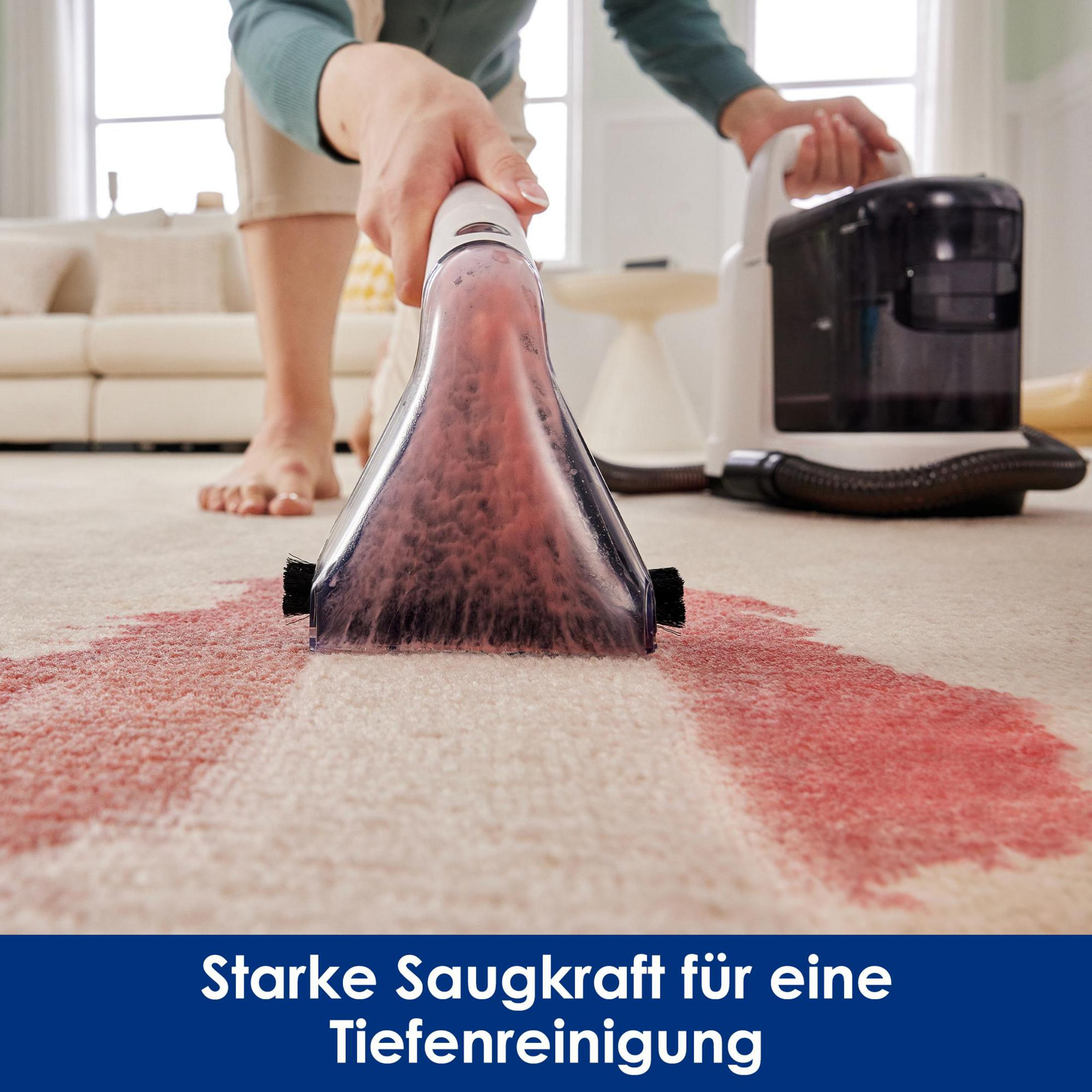 Osoba czyści czerwoną plamę na dywanie odkurzaczem. Odkurzacz jest biało-czarny.