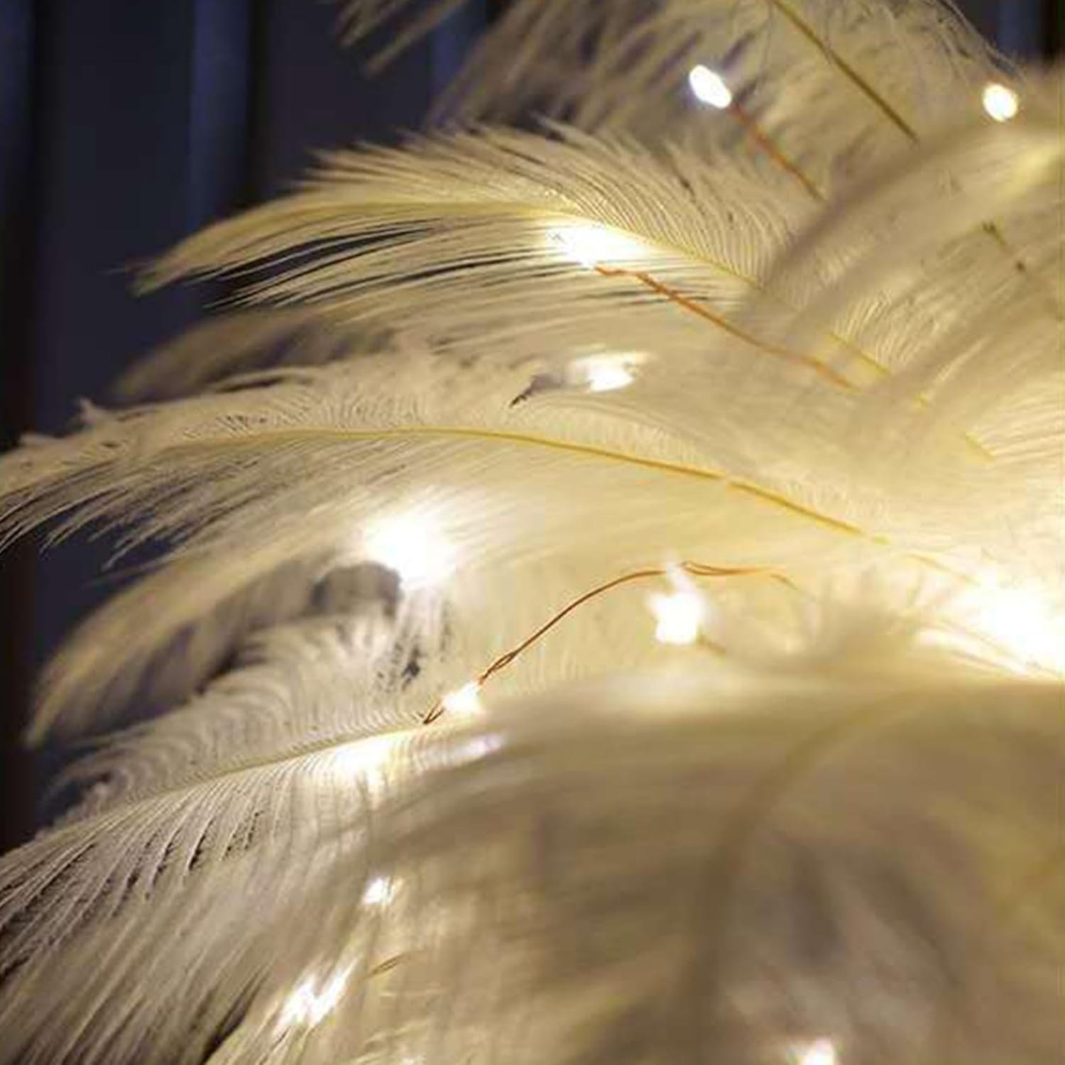 Primer plano de plumas blancas con pequeñas luces en alambre de cobre. El fondo es oscuro. Las plumas son suaves e iluminadas, creando un brillo cálido.