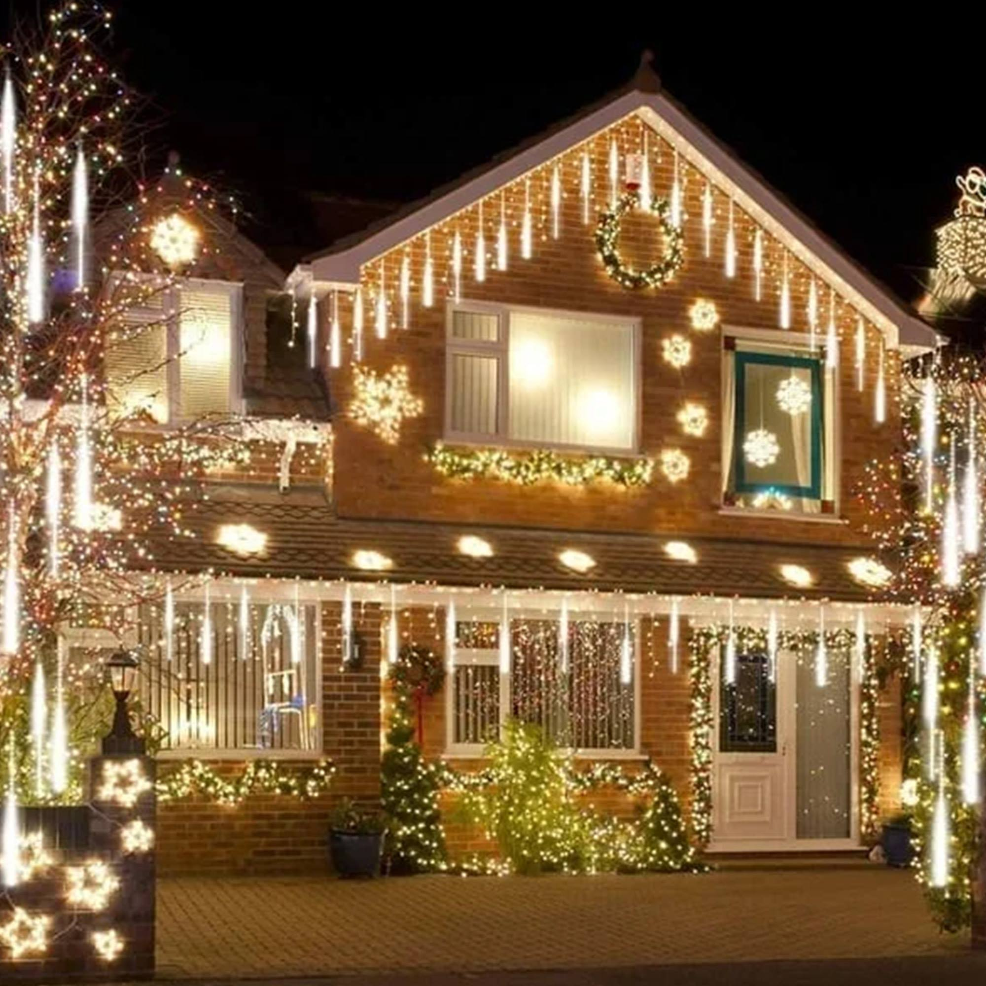 Una casa de noche, decorada con luces navideñas. Luces de carámbanos cuelgan del techo. Luces de copos de nieve en las paredes.