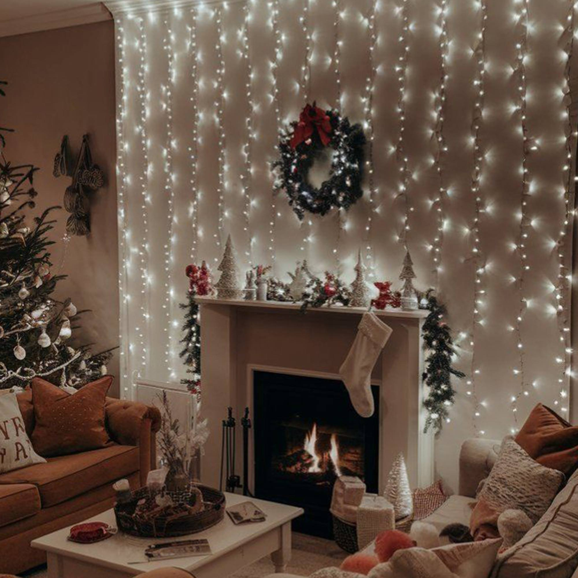 Acogedora escena navideña con árbol decorado, chimenea, luces, corona y guirnalda. Sofás con cojines en primer plano.
