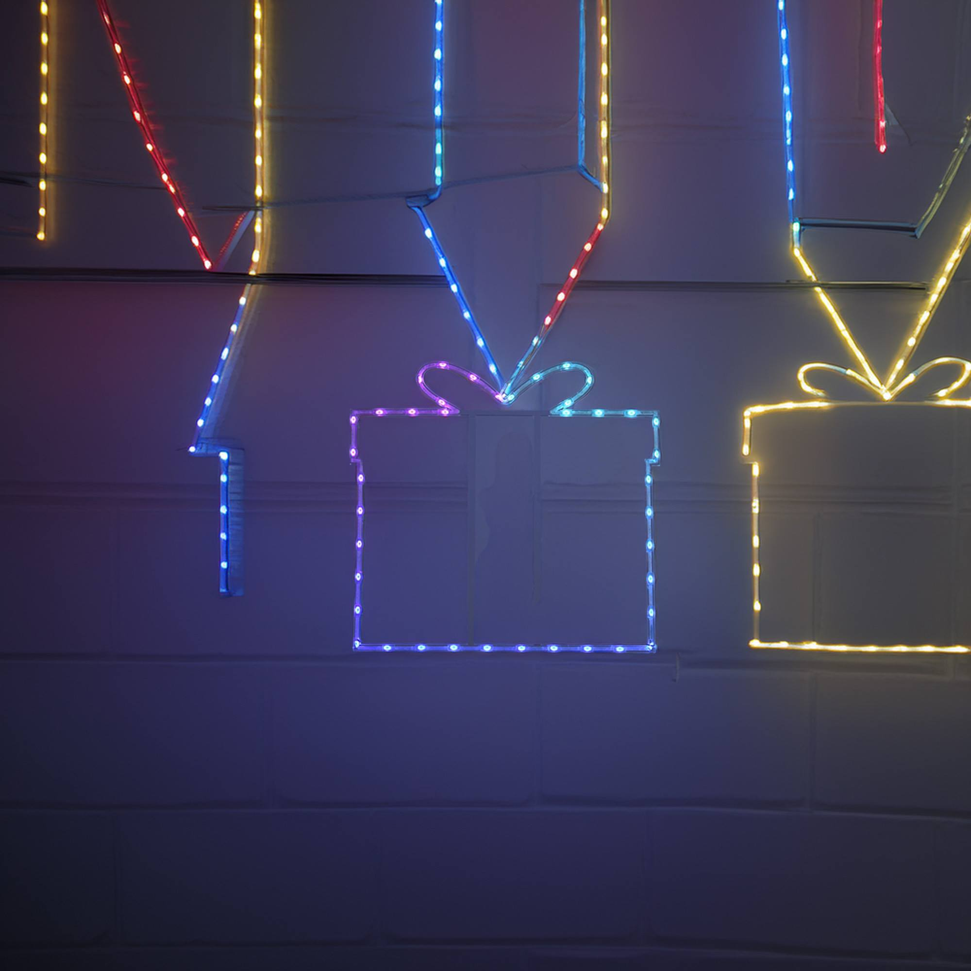 Luces navideñas con forma de cajas de regalo en una pared, con diferentes colores y un fondo oscuro.