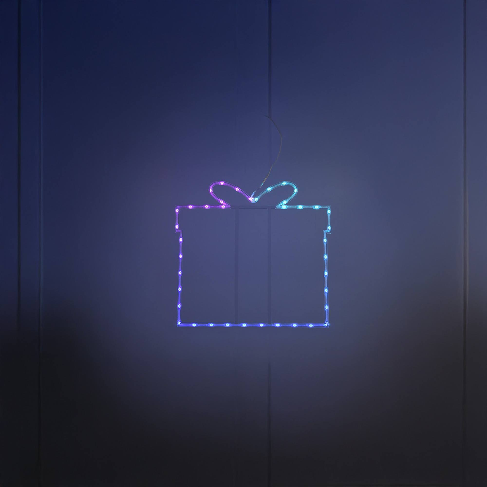 Una lámpara con forma de regalo brillante cuelga contra una pared azul oscuro. La luz está delineada con pequeñas bombillas de colores.