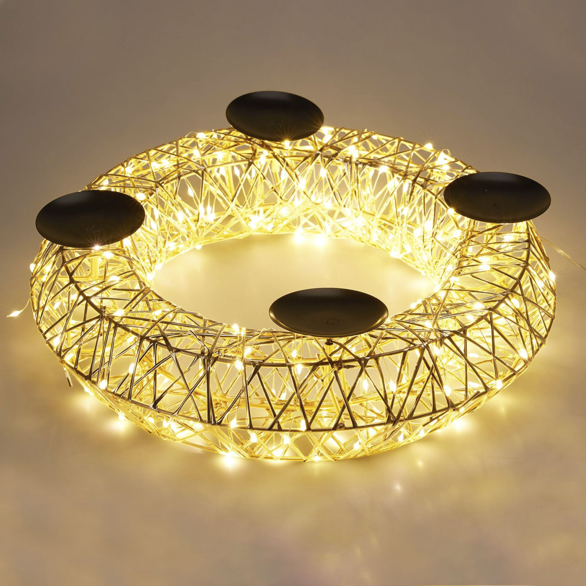 Una corona dorada con luces pequeñas y cuatro candelabros negros sobre un fondo claro.