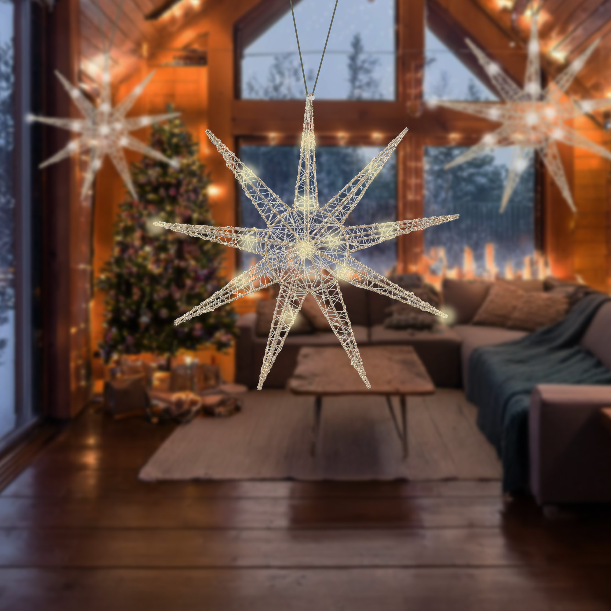 Interior de cabaña con luces en forma de estrella, árbol de Navidad, sofá y chimenea visible por la ventana.