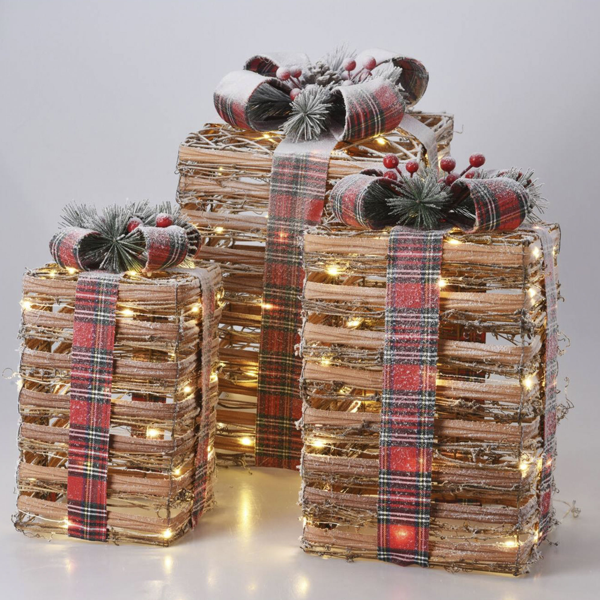 Tres cajas de regalo decorativas de material tejido, adornadas con cintas a cuadros, lazos, detalles escarchados y luces de hadas.