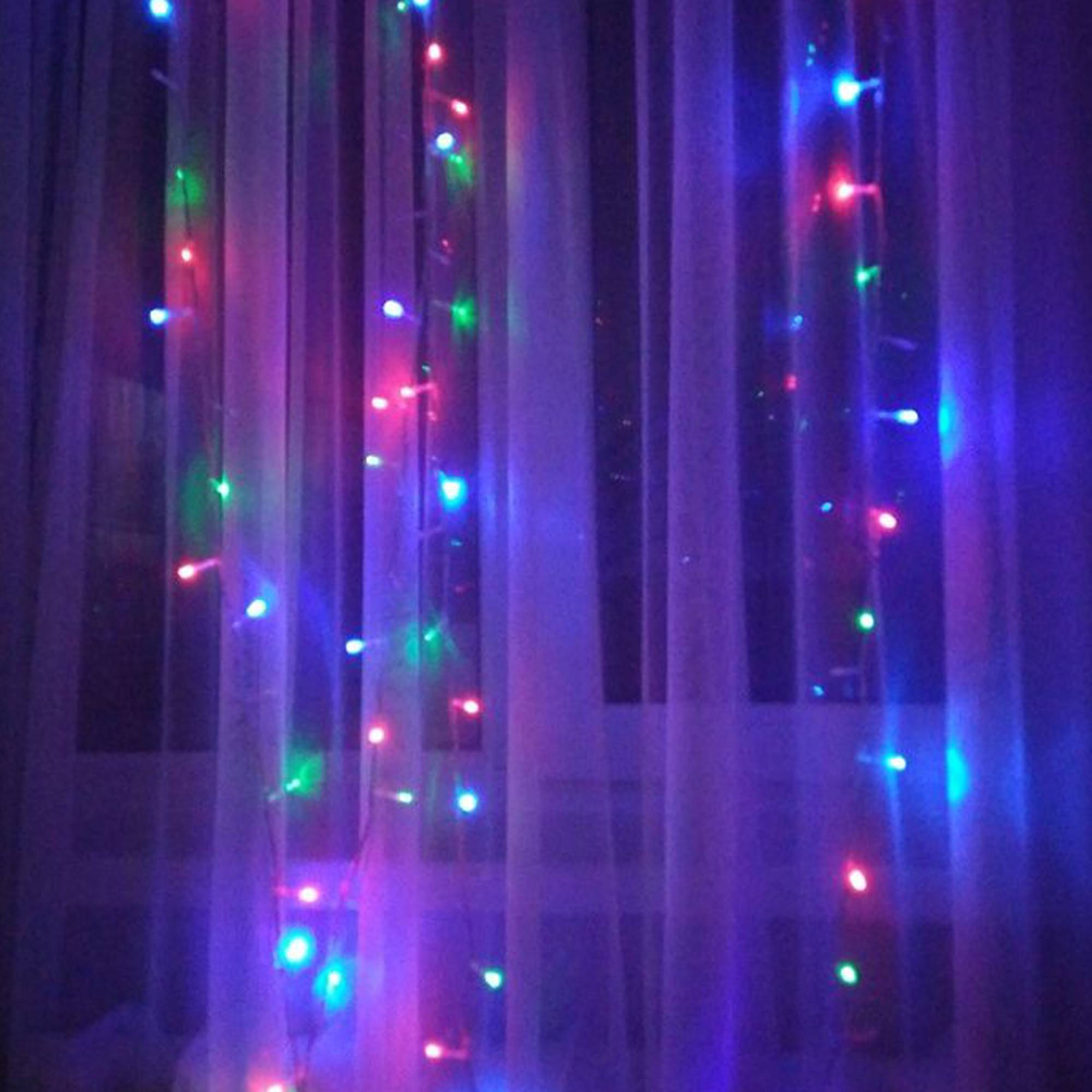 Una cortina iluminada por luces de colores, incluyendo rojo, verde y azul. El fondo es oscuro.