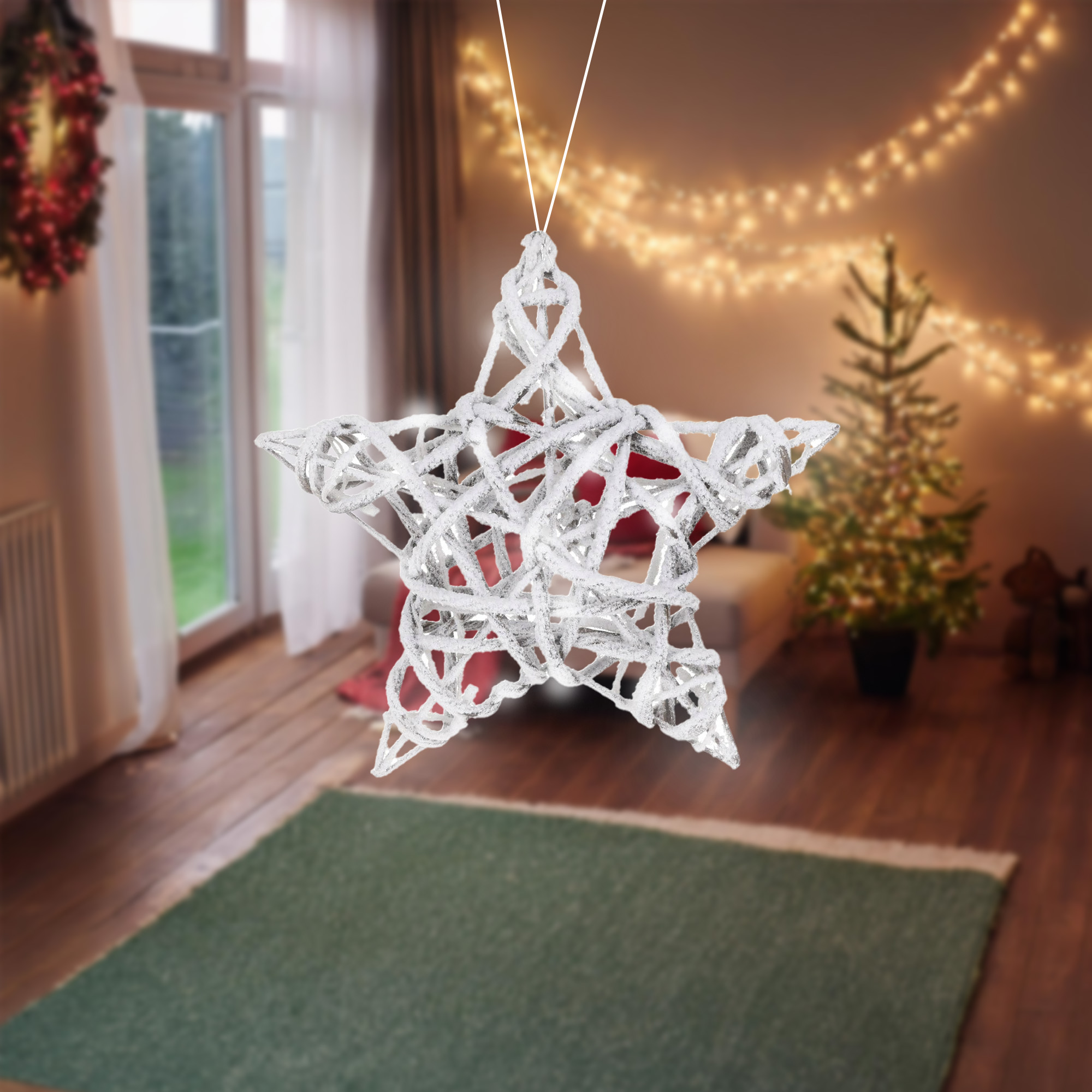 Un adorno de estrella plateada cuelga frente a una habitación con árbol de Navidad, alfombra verde y corona.