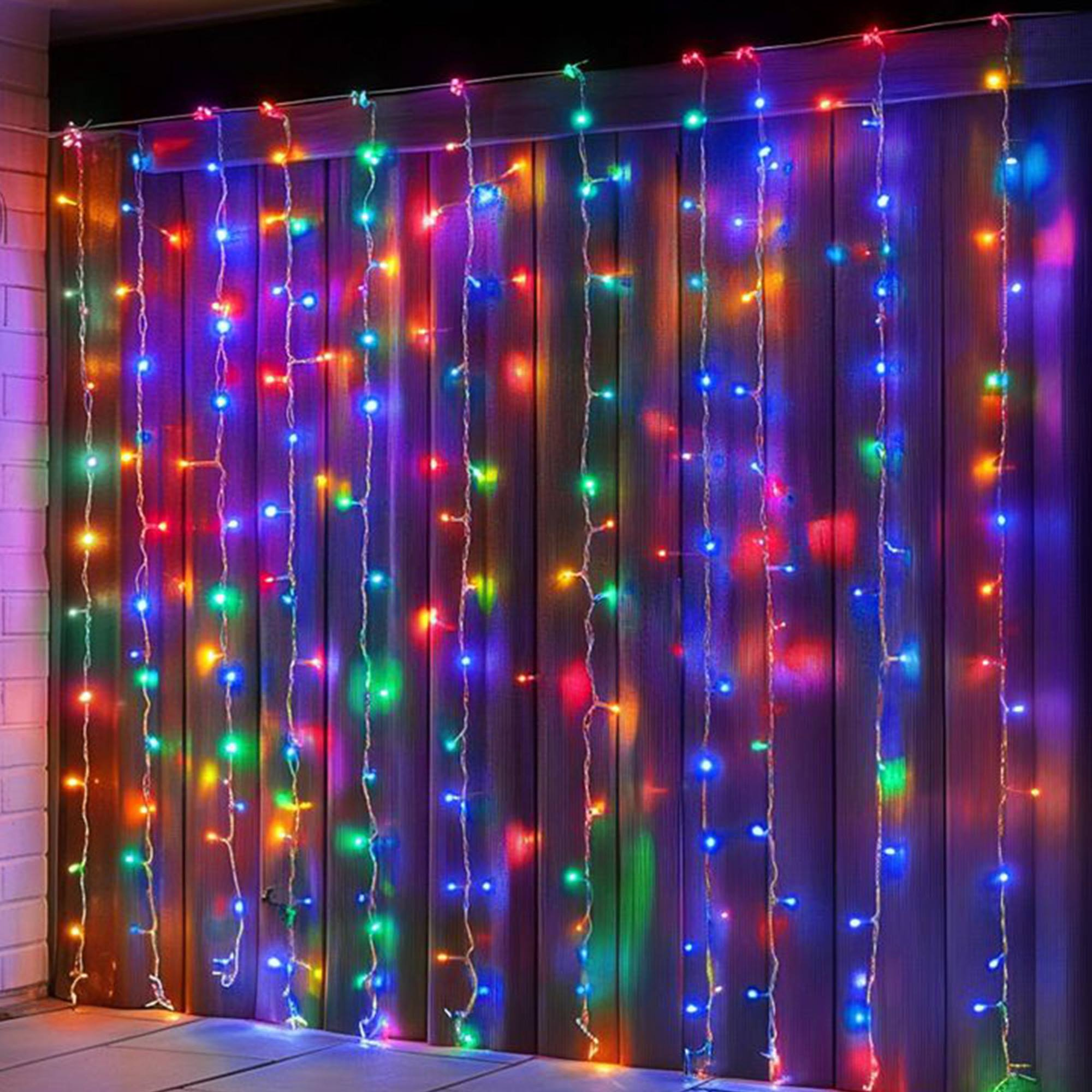 Una cadena de luces LED de colores cuelga frente a una pared de madera. Las luces son rojas, azules, verdes y amarillas.