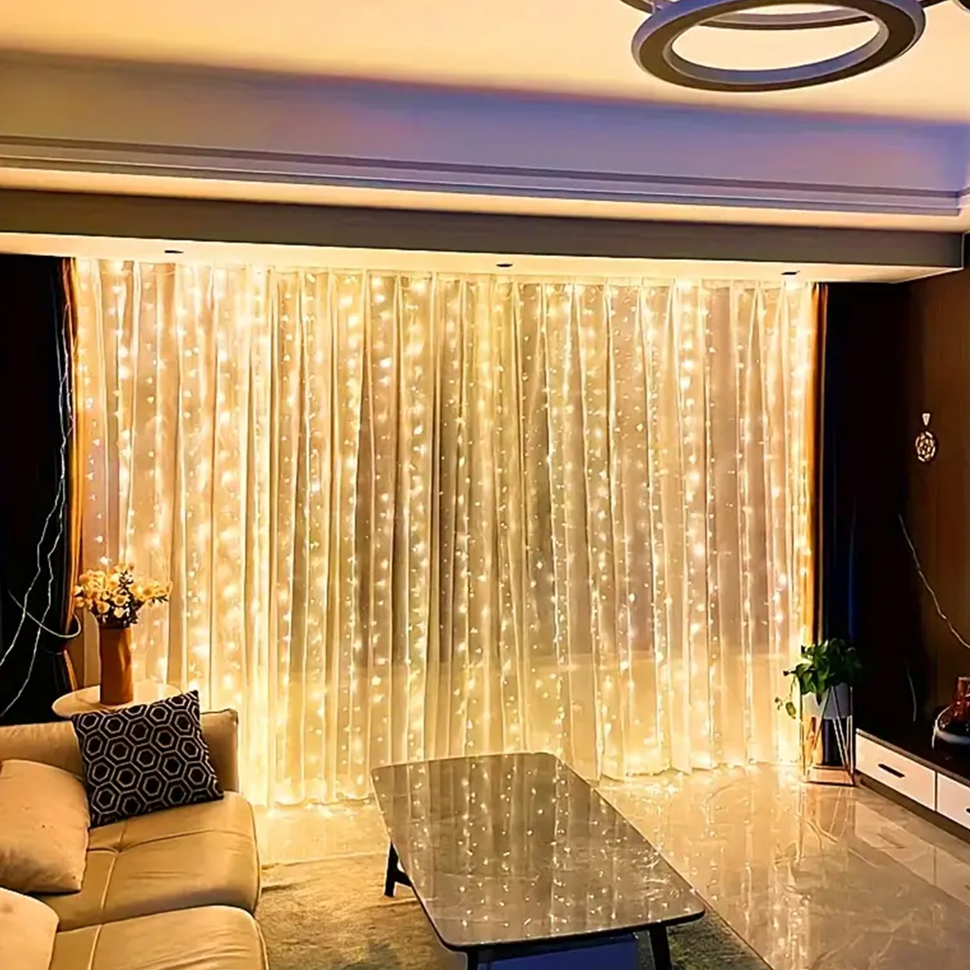 Salón con cortinas de luces, sofá beige, mesa de cristal y una planta. La iluminación cálida crea un ambiente acogedor.