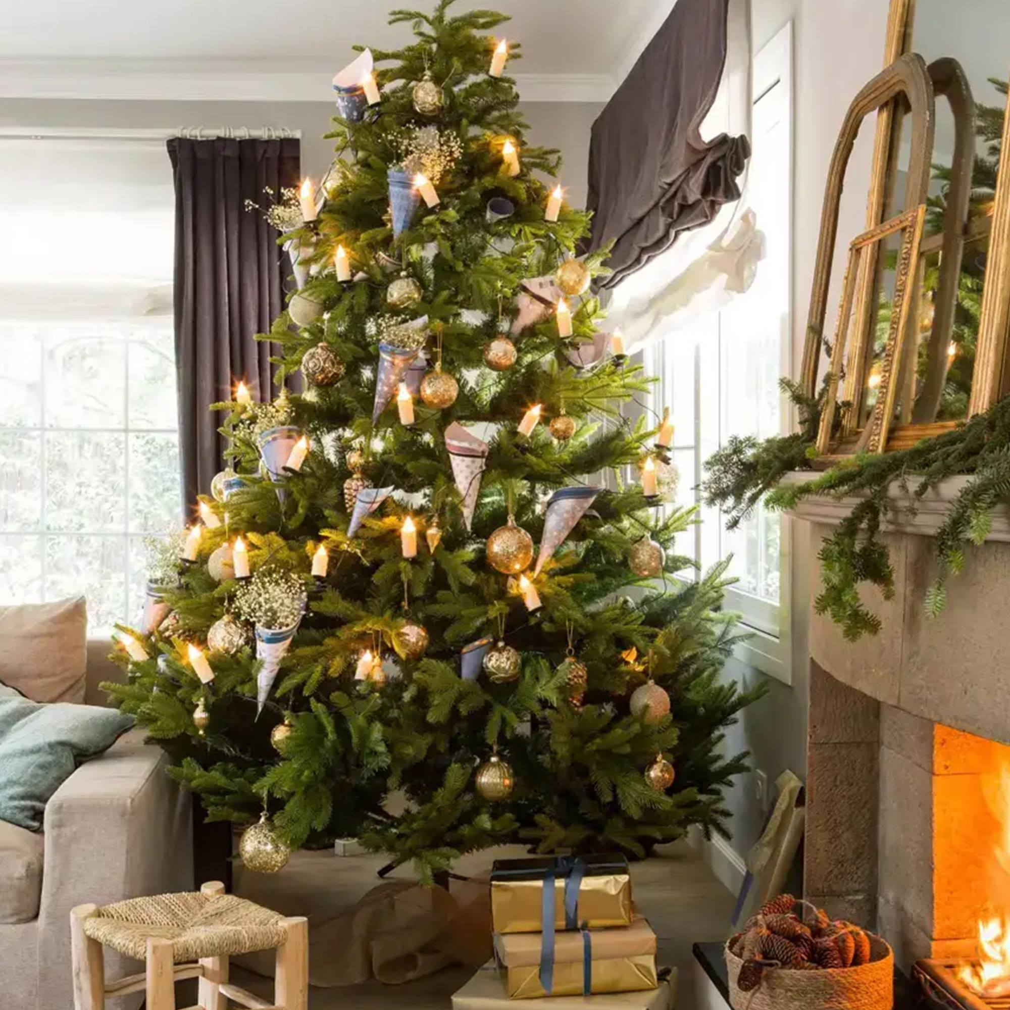 Árbol de Navidad con adornos y luces. Una chimenea está a la derecha. Regalos debajo del árbol. Un sofá y un taburete en la escena.