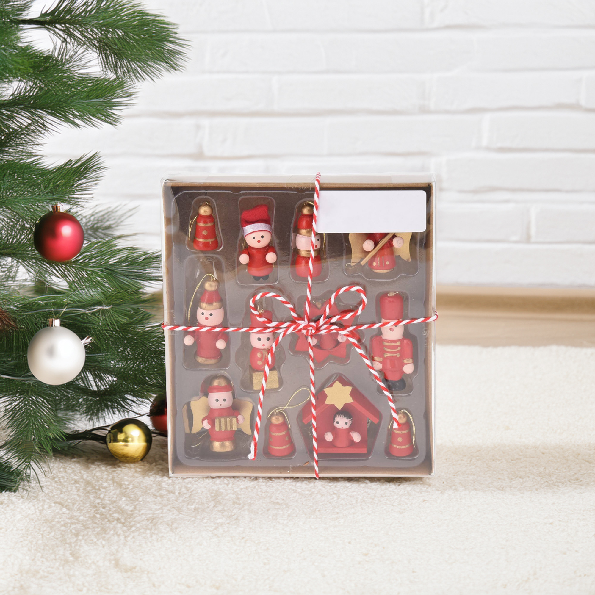 Adornos navideños en una caja, atados con una cuerda roja y blanca, y un árbol de Navidad al fondo.