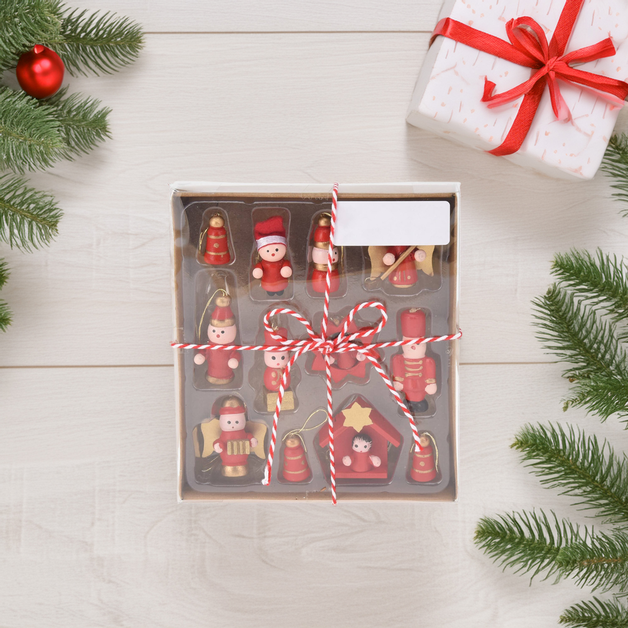 Adornos navideños en una caja, cuerda roja y blanca, regalo con lazo rojo, ramas de abeto, bola roja, sobre una superficie de madera blanca.